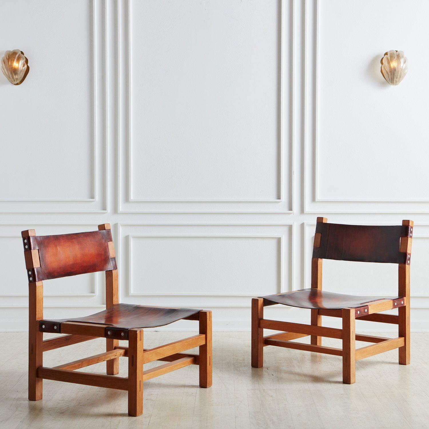 Ein Paar französischer Sessel für den Kamin, zugeschrieben Maison Regain. Die Stühle haben ein Gestell aus Ulmenholz, das mit einer schönen Holzkonstruktion versehen ist, und verfügen über auffallend patinierte Ledersitze und -rückenlehnen. Wir
