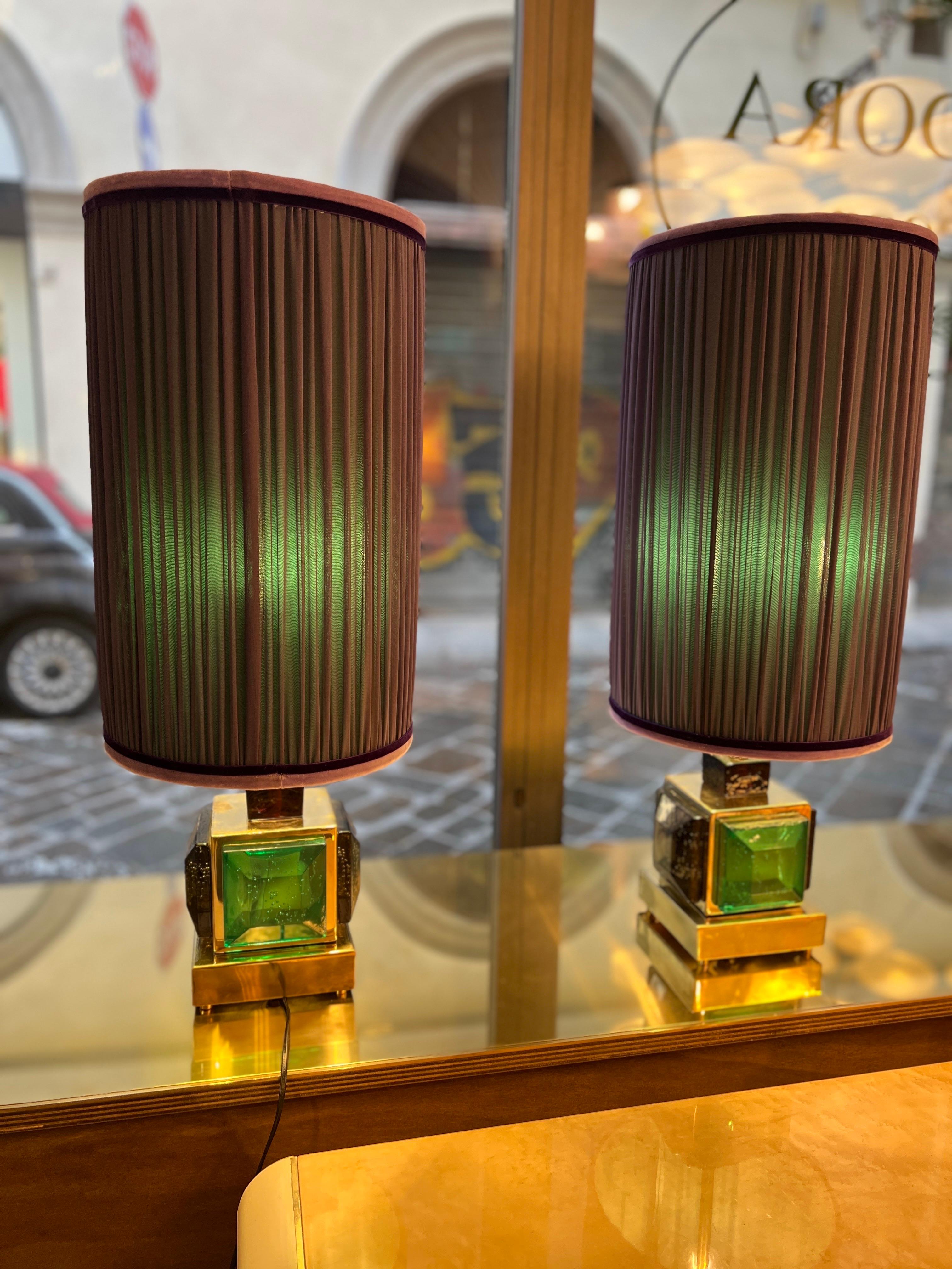 Coppia di lampade da tavolo in vetro di Murano e ottone color verde smeraldo con paralumi cuciti a mano a doppia tonalità. Ogni lampada presenta una base cubica in ottone sormontata da un elemento in vetro di Murano a forma di diamante. Le quattro