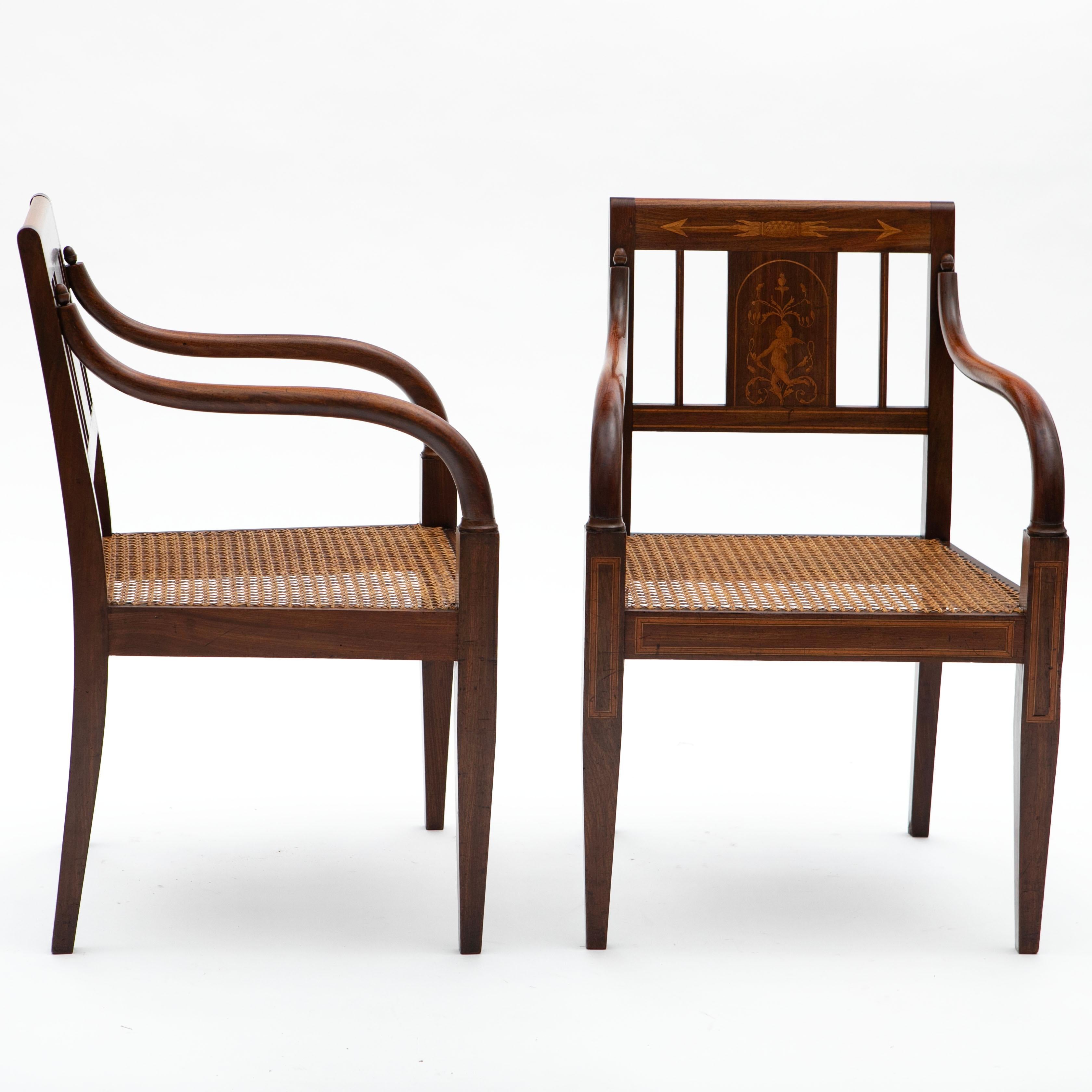 A stunning pair of Empire armchairs from Copenhagen, circa 1810, made from solid mahogany with intricate satinwood inlays on the backrest, apron, and front legs.
The chairs feature tapered legs and their original cane seats, which are in excellent