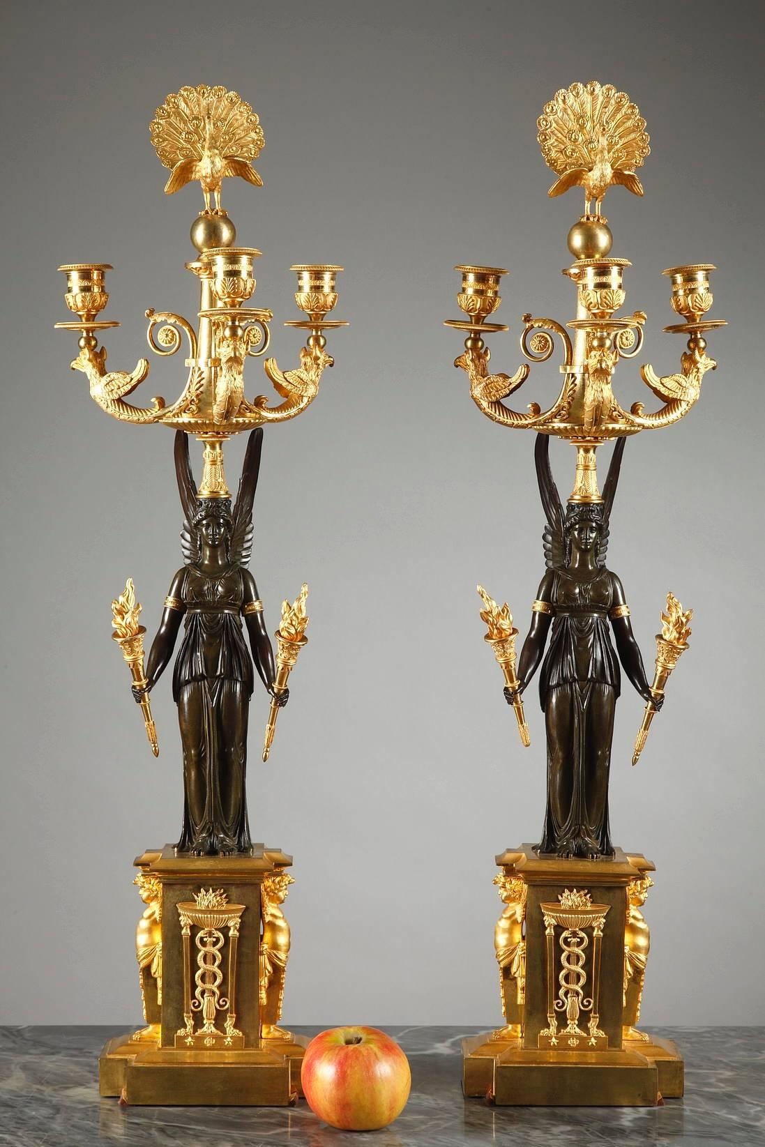 Impressive pair of gilt and sculpted bronze candelabras with three branches. The stem of each candelabrum is a patinated bronze form of the winged goddess, Victory, who holds a gilt bronze torch in each of her hands. Her head is topped with a gilt