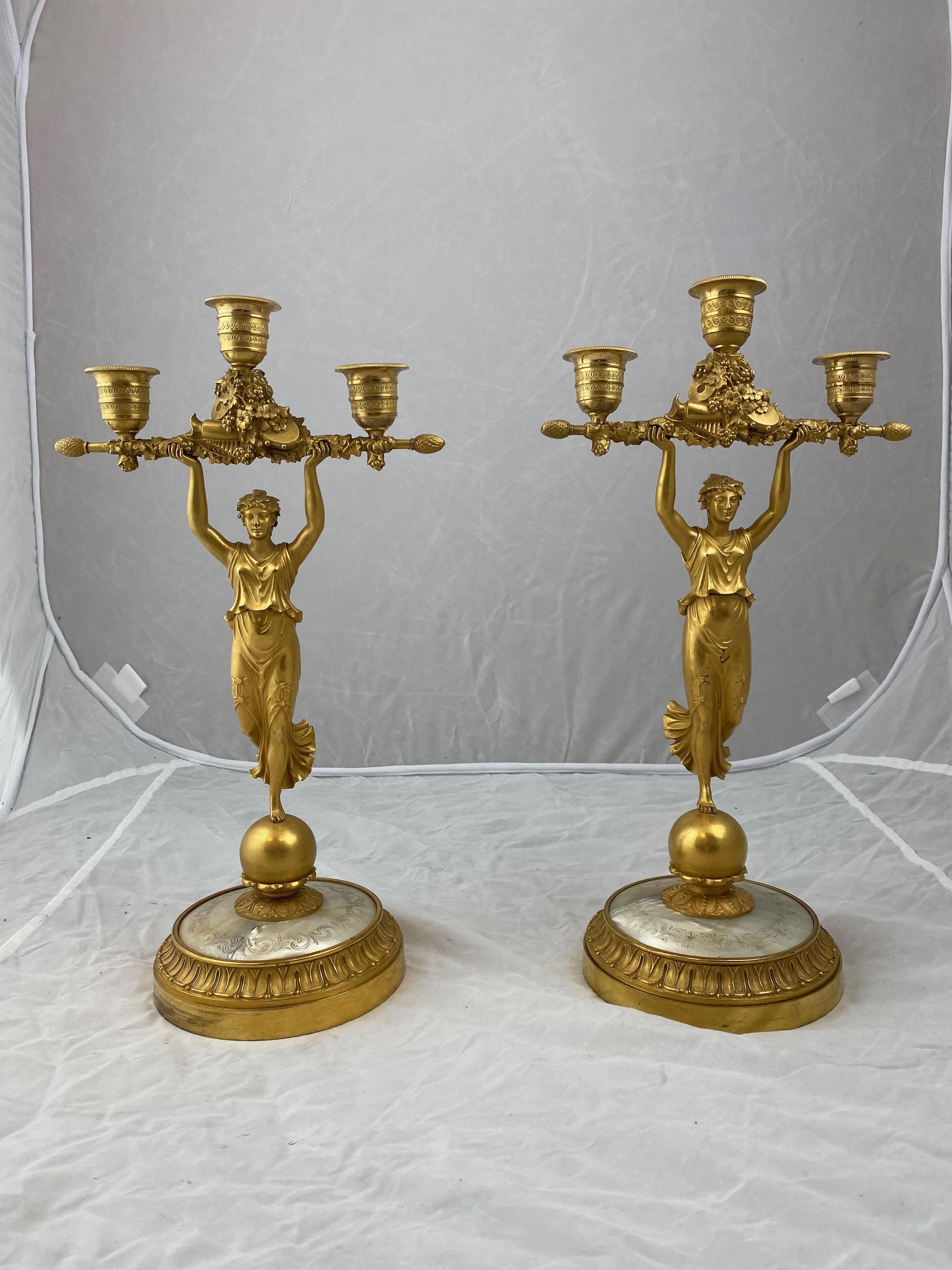 An unusual model with a Classic female figure standing holding a bar with three candleholders on it. The candelabra are made of gilt bronze and the feet are covered with ornamented mother of pearl.