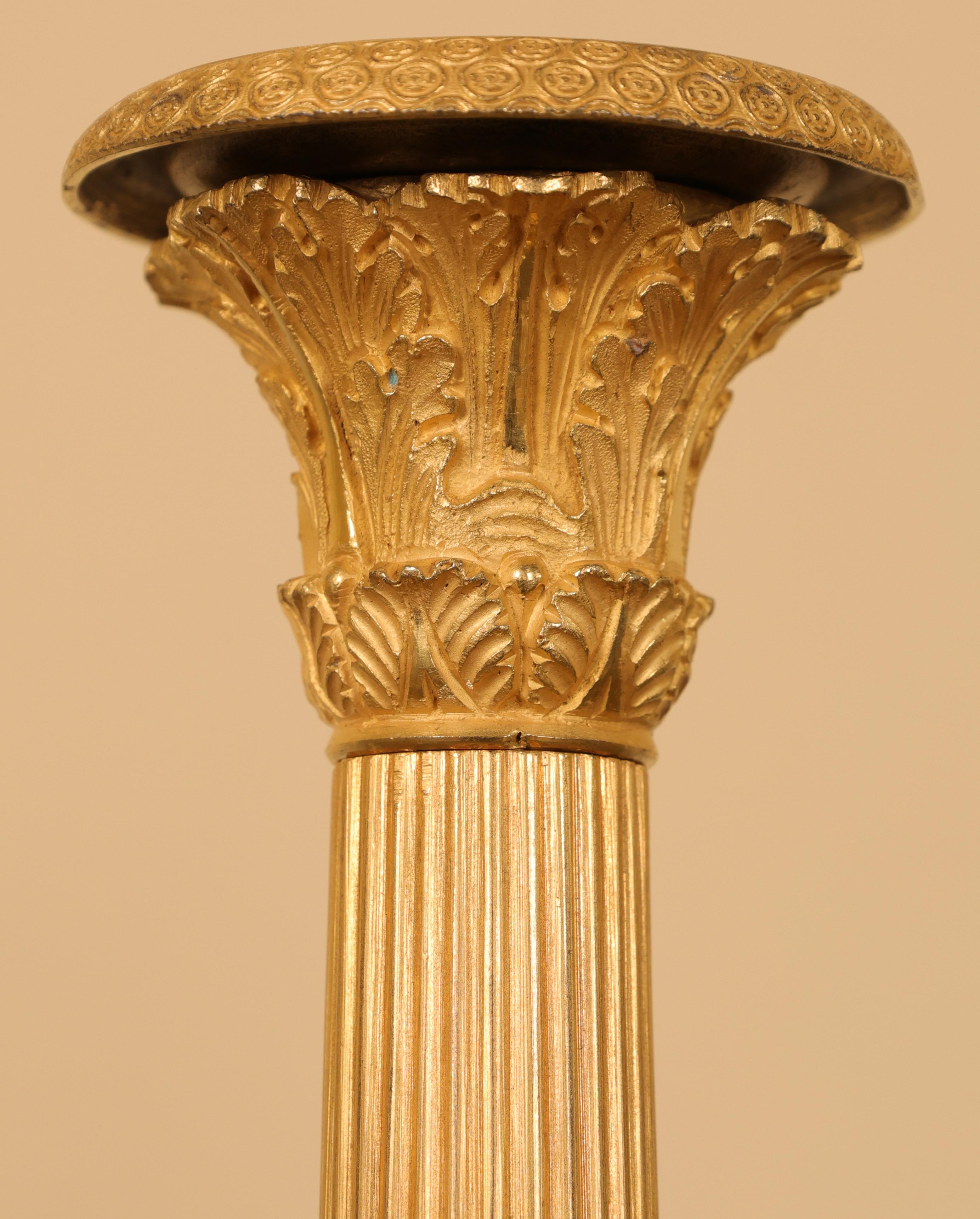 Coppia di candelieri Impero francesi dorati e bruniti con collare chiaro. I gambi sono scanalati e decorati con foglie d'acanto.