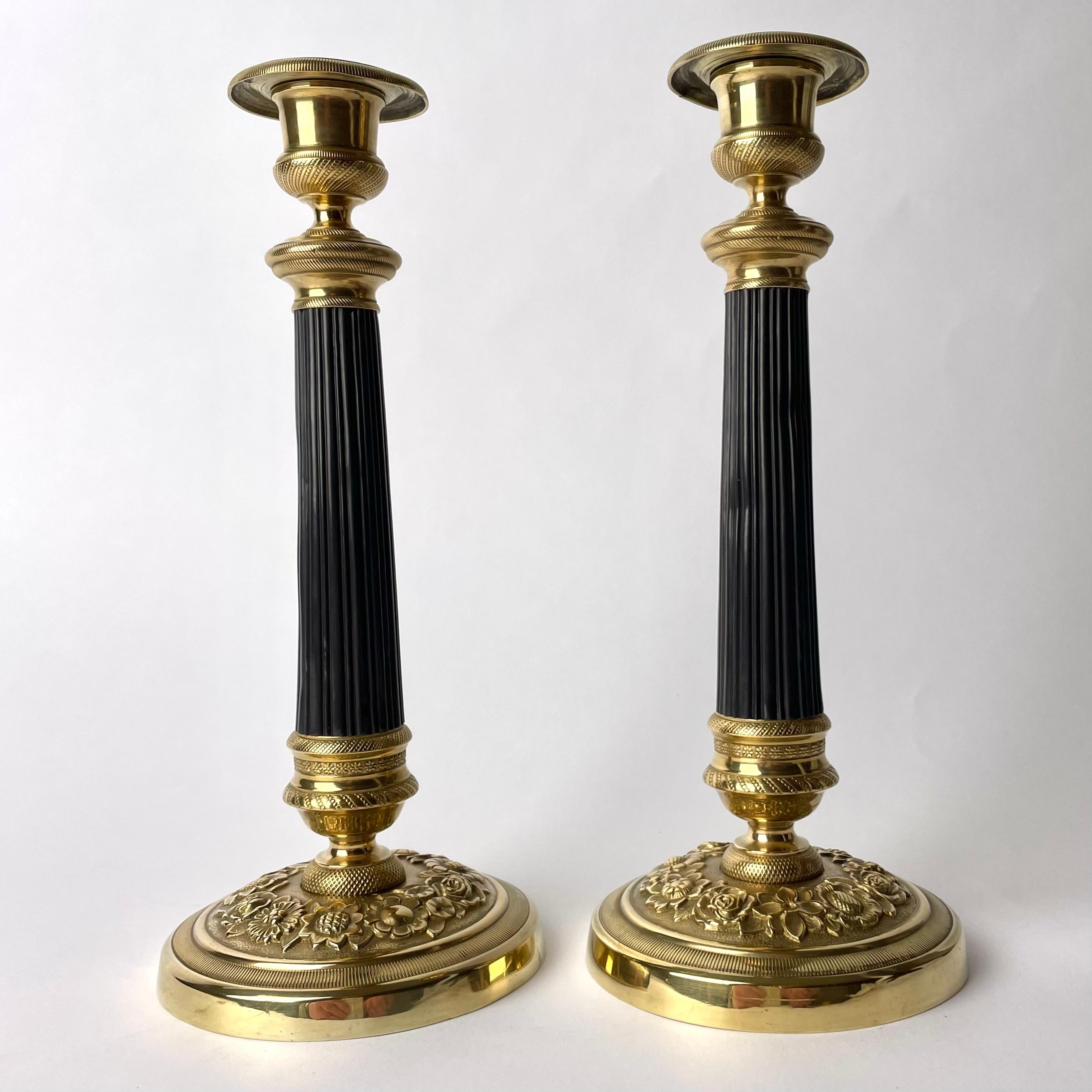 Paar Empire-Kerzenleuchter aus vergoldeter und dunkel patinierter Bronze. Hergestellt in Frankreich in den 1820er Jahren. Schön verziert mit Blumen und einer dunkel patinierten Säule in der Mitte des Leuchters.

Abnutzung entsprechend dem Alter und