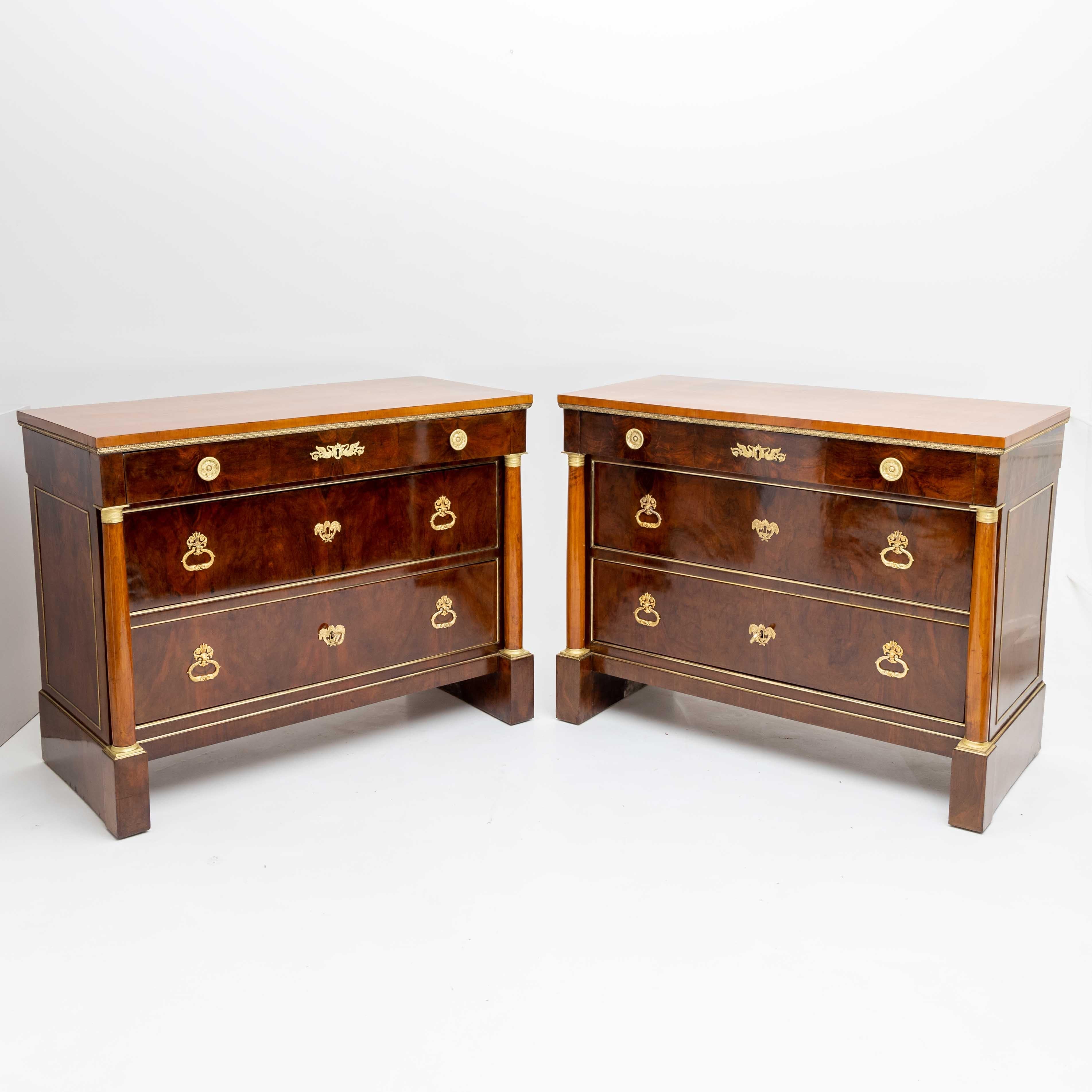 This pair of Empire chest of drawers showcases three drawers, accompanied by lateral columns adorned with fire-gilt bronze bases and capitals. Notably, the top drawer extends slightly, finding support on the columns themselves. Standing on the