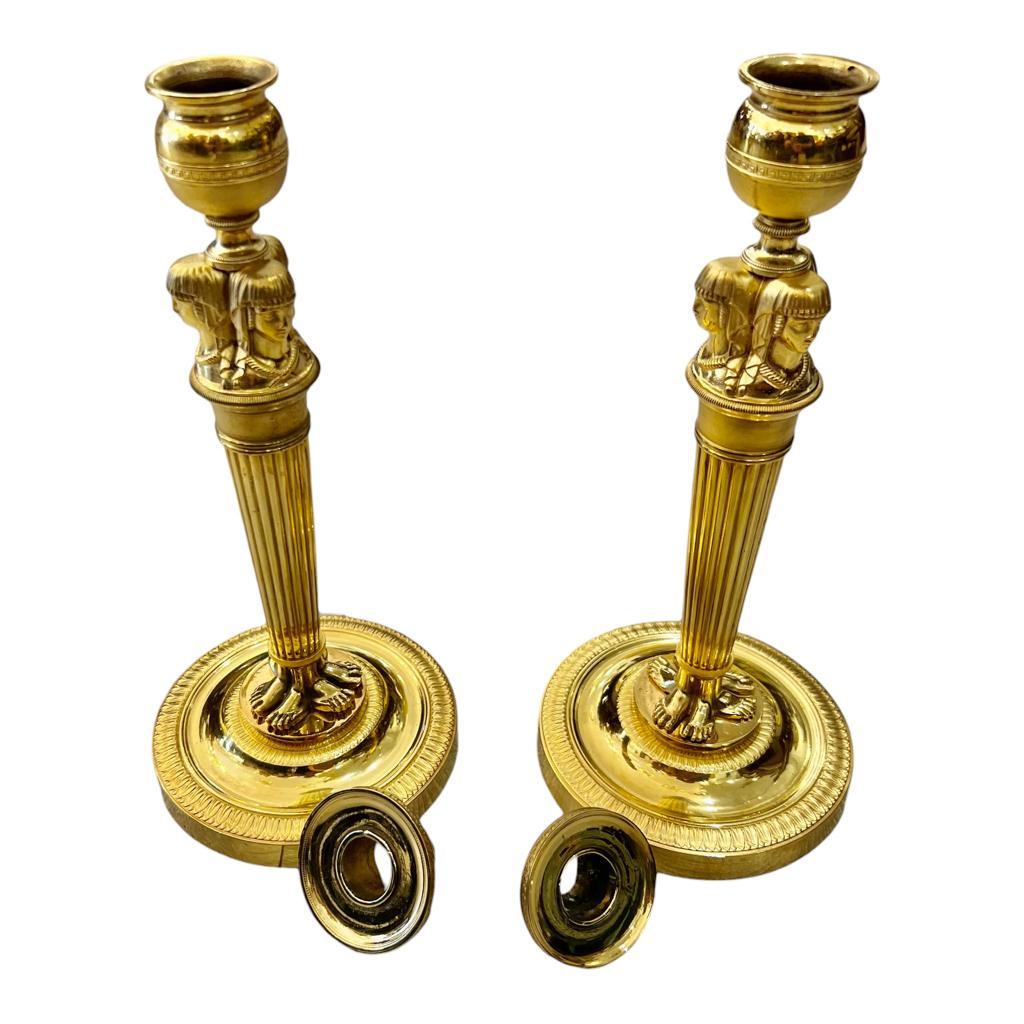 A fine pair of candlesticks in gilt bronze or molybdenum from the Empire period, adorned with three Egyptian caryatids, attributed to the renowned French gilder Claude Galle (1759-1815). The ball-shaped nozzles of the candlesticks rest on three