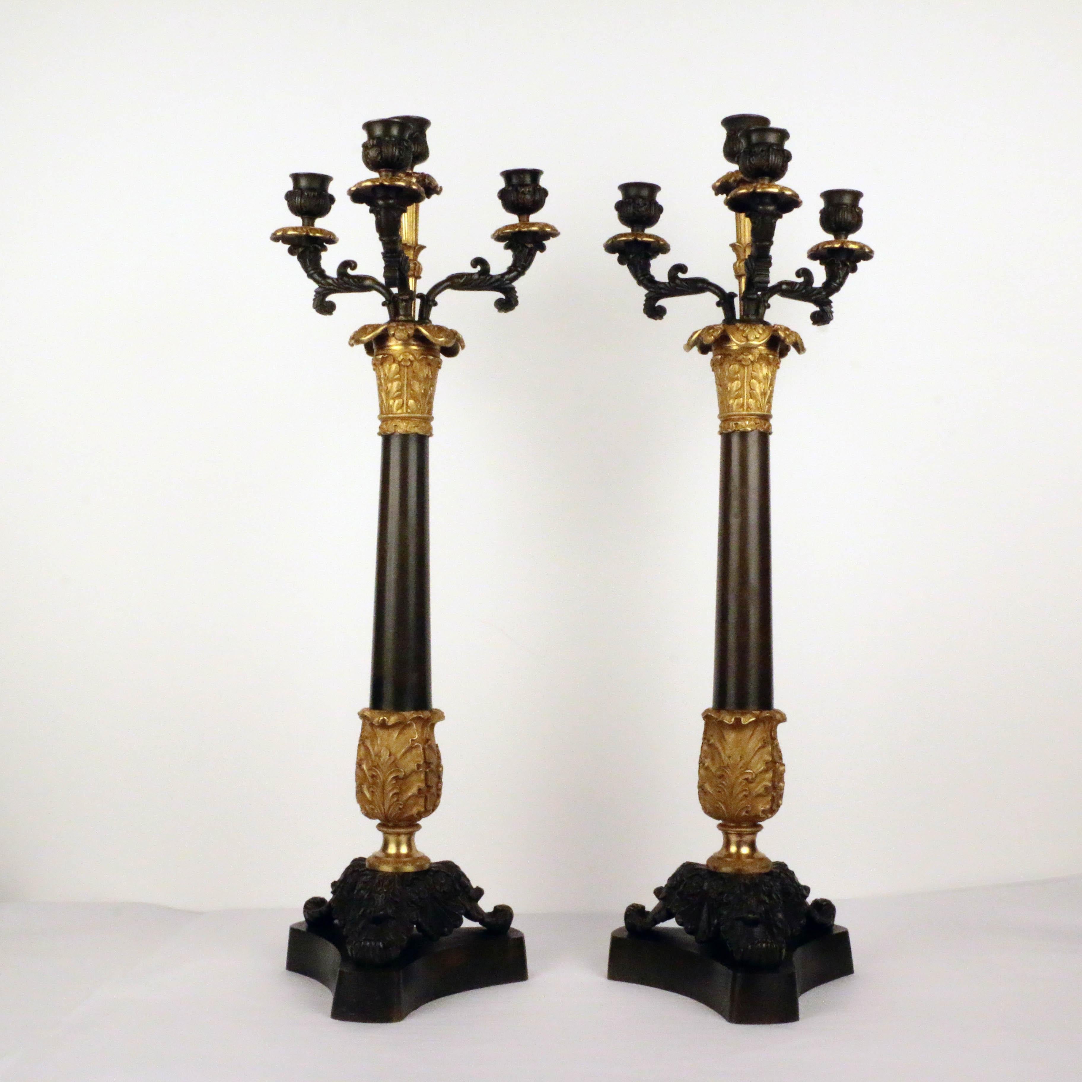 Pair of Empire period parcel-gilt and patinated bronze four-light candelabra, the patinated column raised on triform scrolled feet over incurved plinth supporting a gilt bronze standard with urn form patinated candle cups, flanked by scrolling