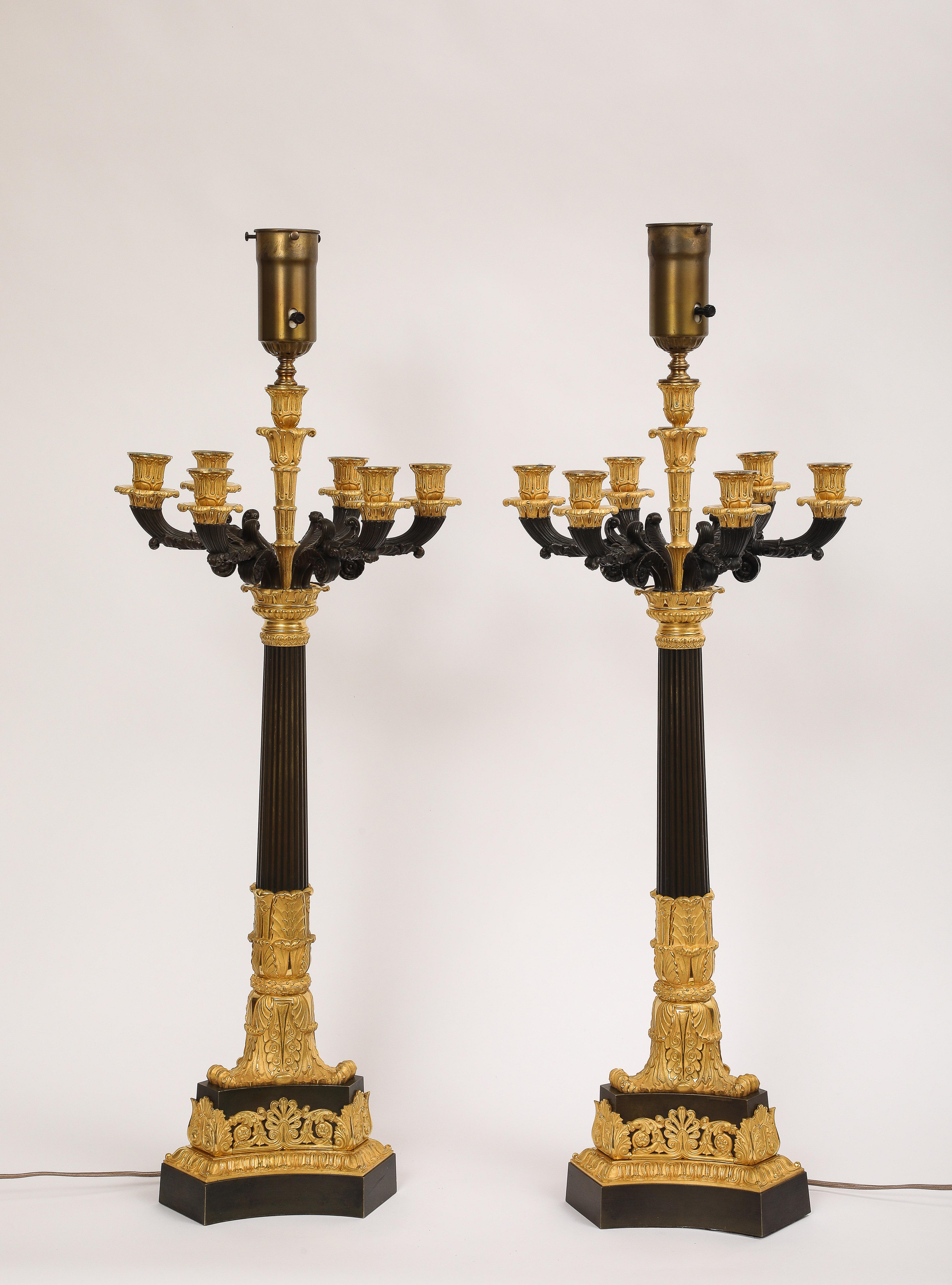 Ein auffälliges und fein gegossenes Paar mehrarmiger französischer Empire-Kandelaber aus den frühen 1800er Jahren, ausgeführt in einer raffinierten Kombination aus Ormolu und patinierter Bronze und jetzt diskret als Lampen umfunktioniert. Im Zentrum