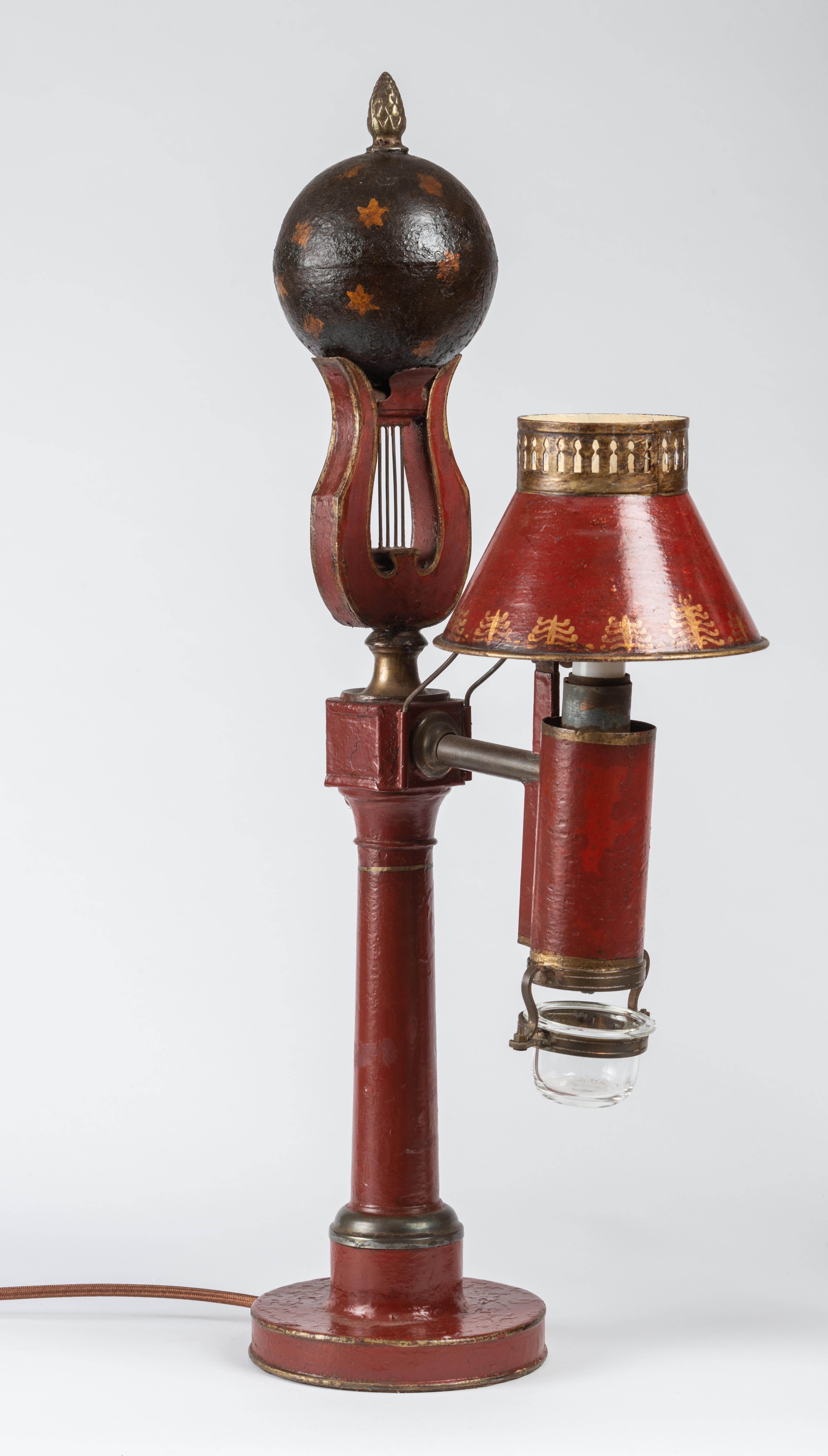 The red tole lamps with shades decorated with palms and ending in a lyre topped by a sphere painted with stars. With the original glass cups which would have caught the oil drip. Electrified.
The English version of the Quinquet lamp is the argand