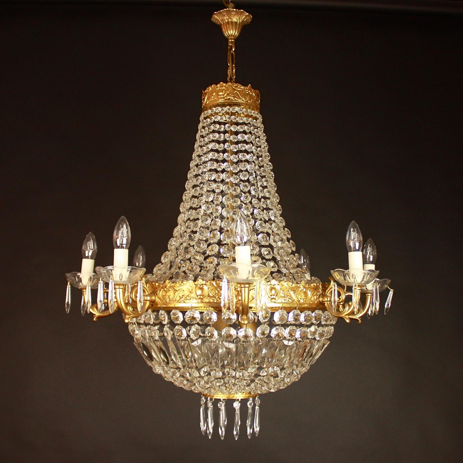 A pair of Empire style chandeliers, each with a bronze cast corona hang with suspended chains of graduated octagonal flatback beads, with a central gilt bronze tier depicting acanthus leaves, scrolls and rocaille ornaments and supporting eight