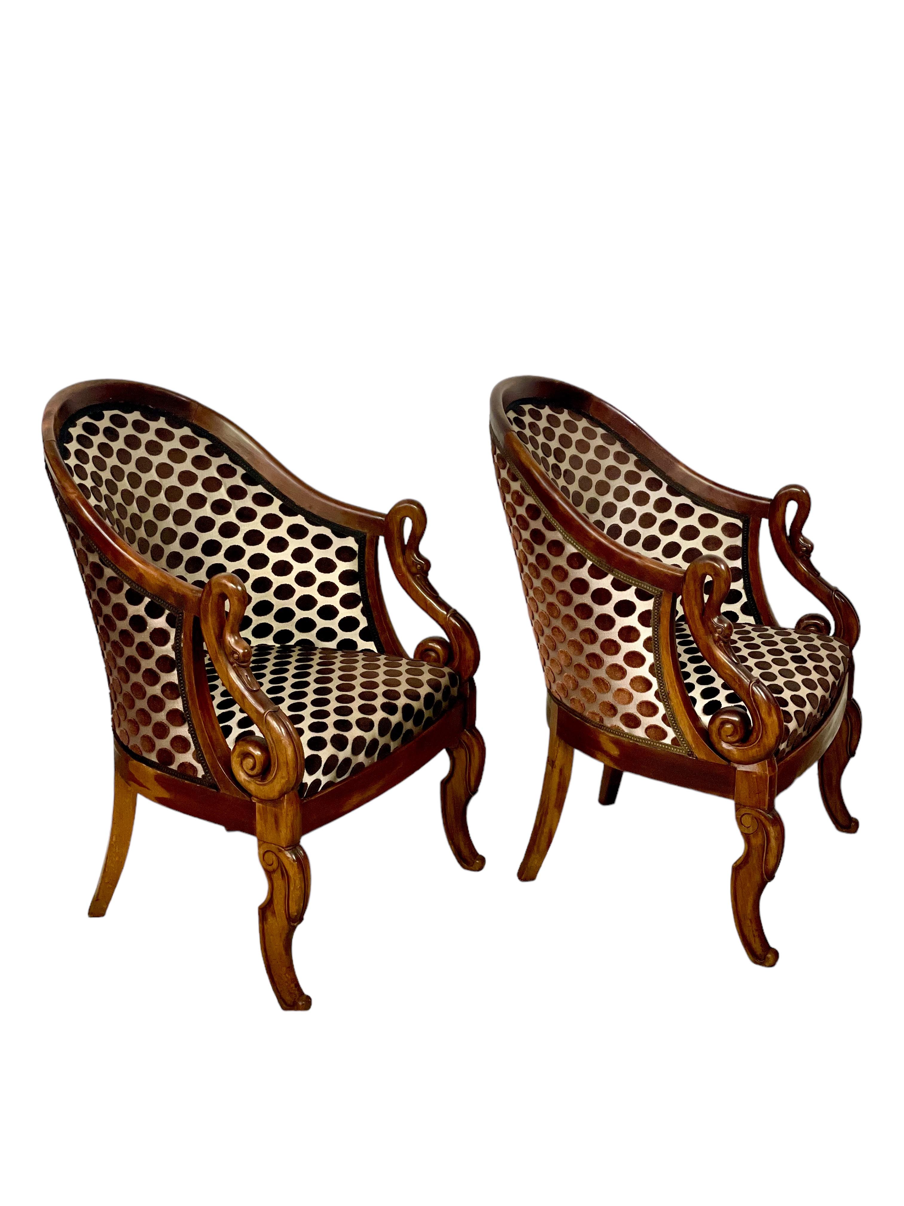 Cette paire de chaises Bergères de style Empire, datant du début du 20e siècle, rehausse votre intérieur. Ces élégants fauteuils sont dotés de dossiers en forme de gondole gracieusement incurvés et d'accoudoirs en col de cygne, offrant un confort