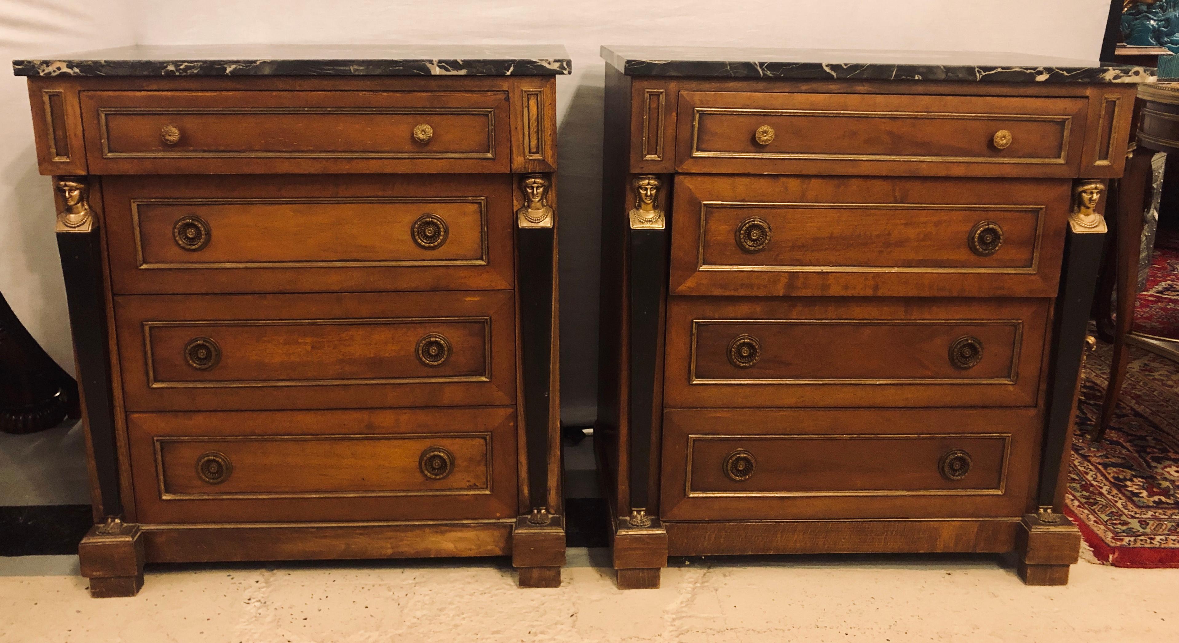 Pair of Empire style bronze mounted commodes or nightstands or end tables. The pair with black marble tops under four bronze framed drawers flanked by ebony bodied full figured ladies with bronze busts and feet. In good condition.