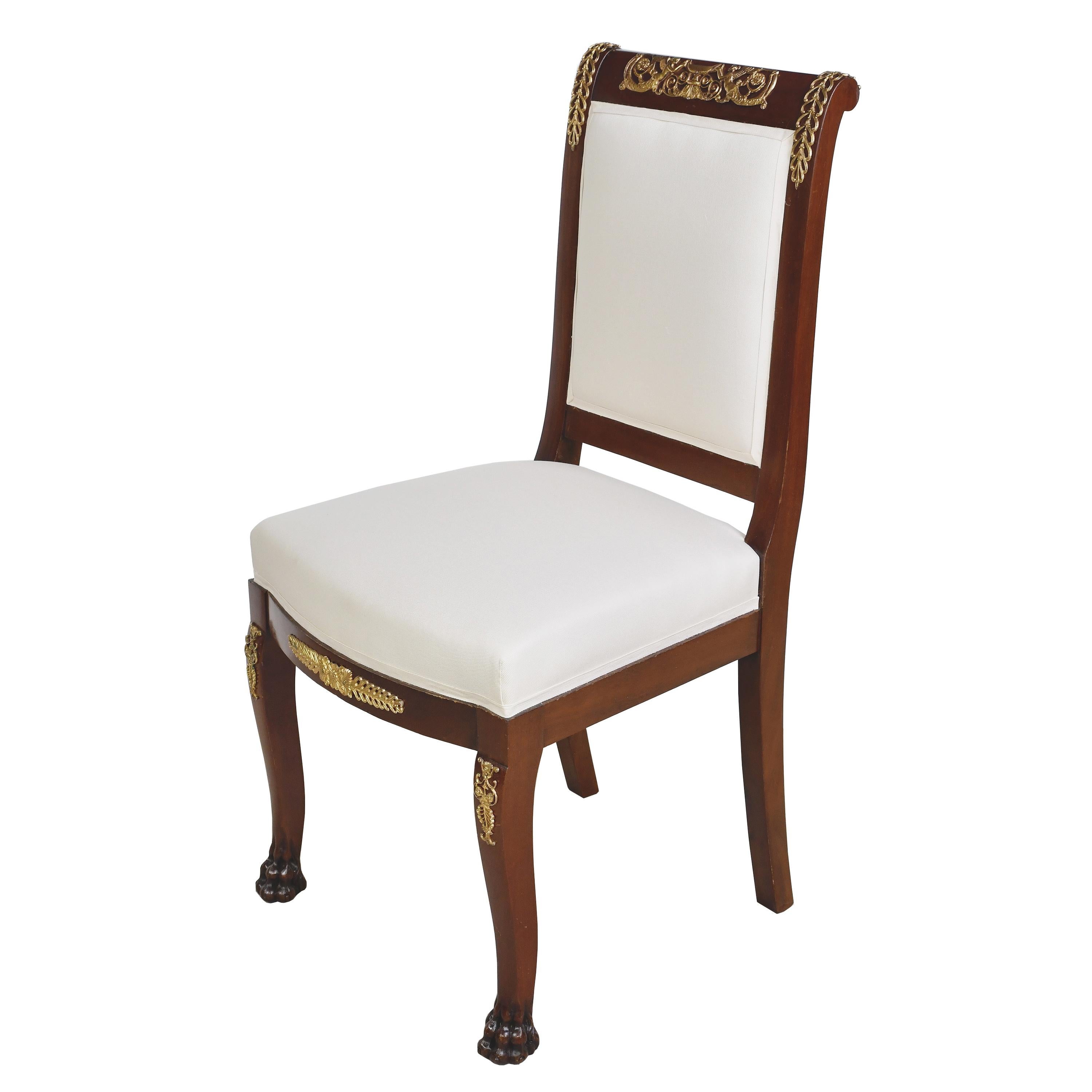 A handsome pair (2) of French Empire-style dining or salon chairs in an auburn brown-colored mahogany with upholstered square back & upholstered serpentine seat. Bronze doré ormolu mounts embellish the frame, with winged female figures holding an