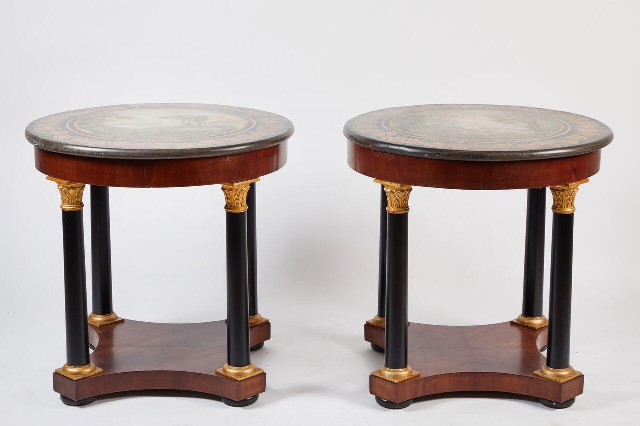 Pair of round Empire style mahogany gueridon. The hand-painted tops which feature charming pastoral scenes are supported by ebonized columns with gilt capitals and bases. These would be wonderful used as side tables at a sofa in a living room or