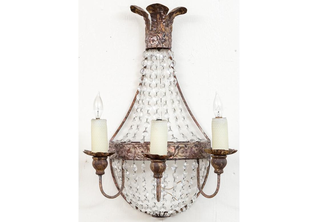 The pair of wall sconces in the Empire style with embossed gilt metal having a floral-like design, three electrified lights with beeswax candle covers. The sconces with drapes of faceted crystal beads.
Dimensions: 17