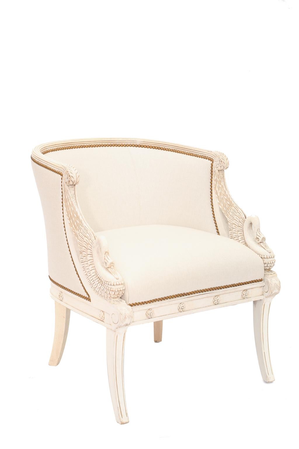 Pair of upholstered bergeres, in the manner of Jacob Freres, each having a painted frame with natural wear, its tub form, with a padded back in reeded frame, downswept arms are carved into intricate winged swans, ending in scrolls, its crown seat on