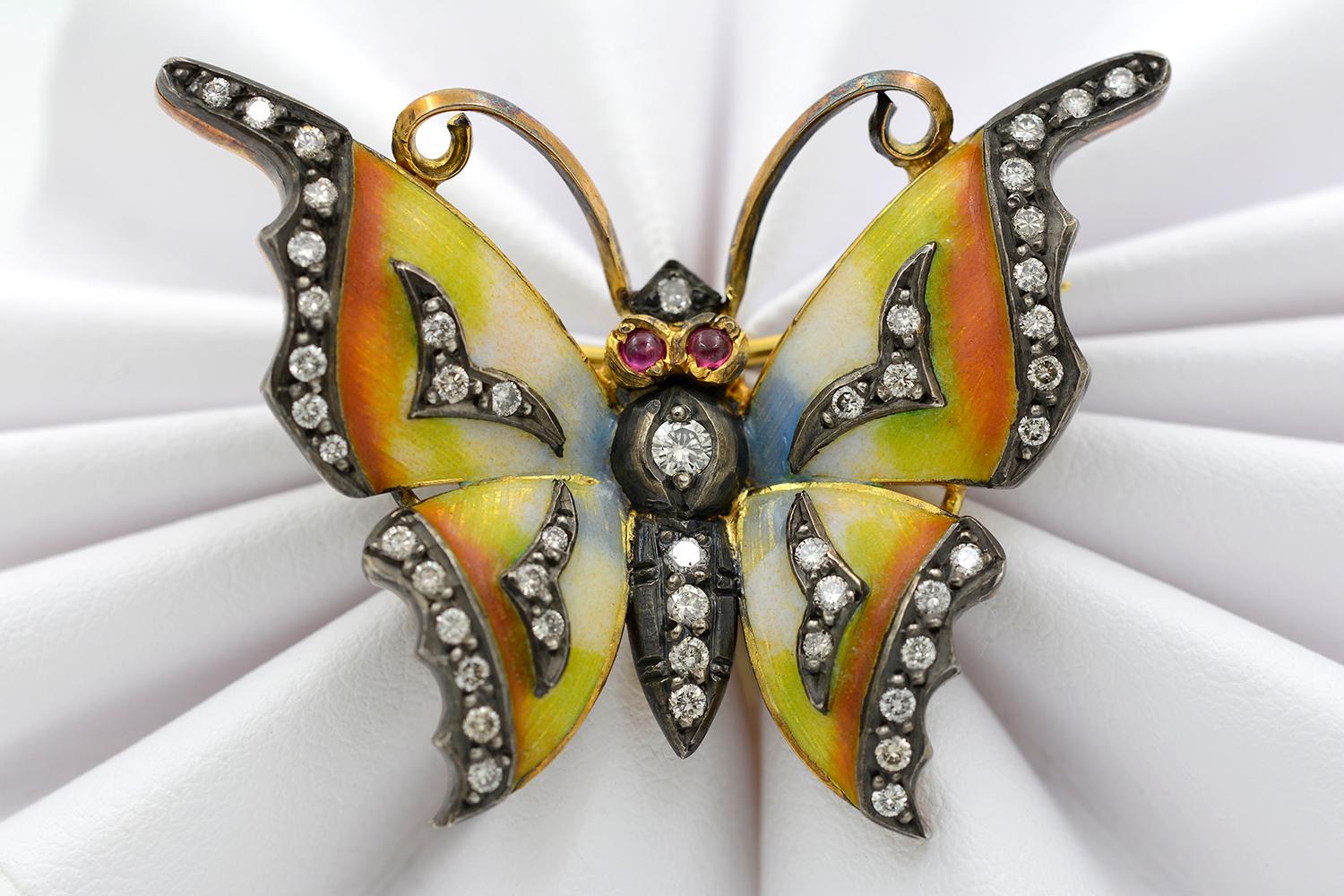 This charming Arts & Crafts style enamel butterfly pin is crafted from 18 karat yellow gold. The pin features yellow and orange enamel set with 30 round brilliant cut diamonds weighing approximately 0.65 carats combined and two cabochon rubies for