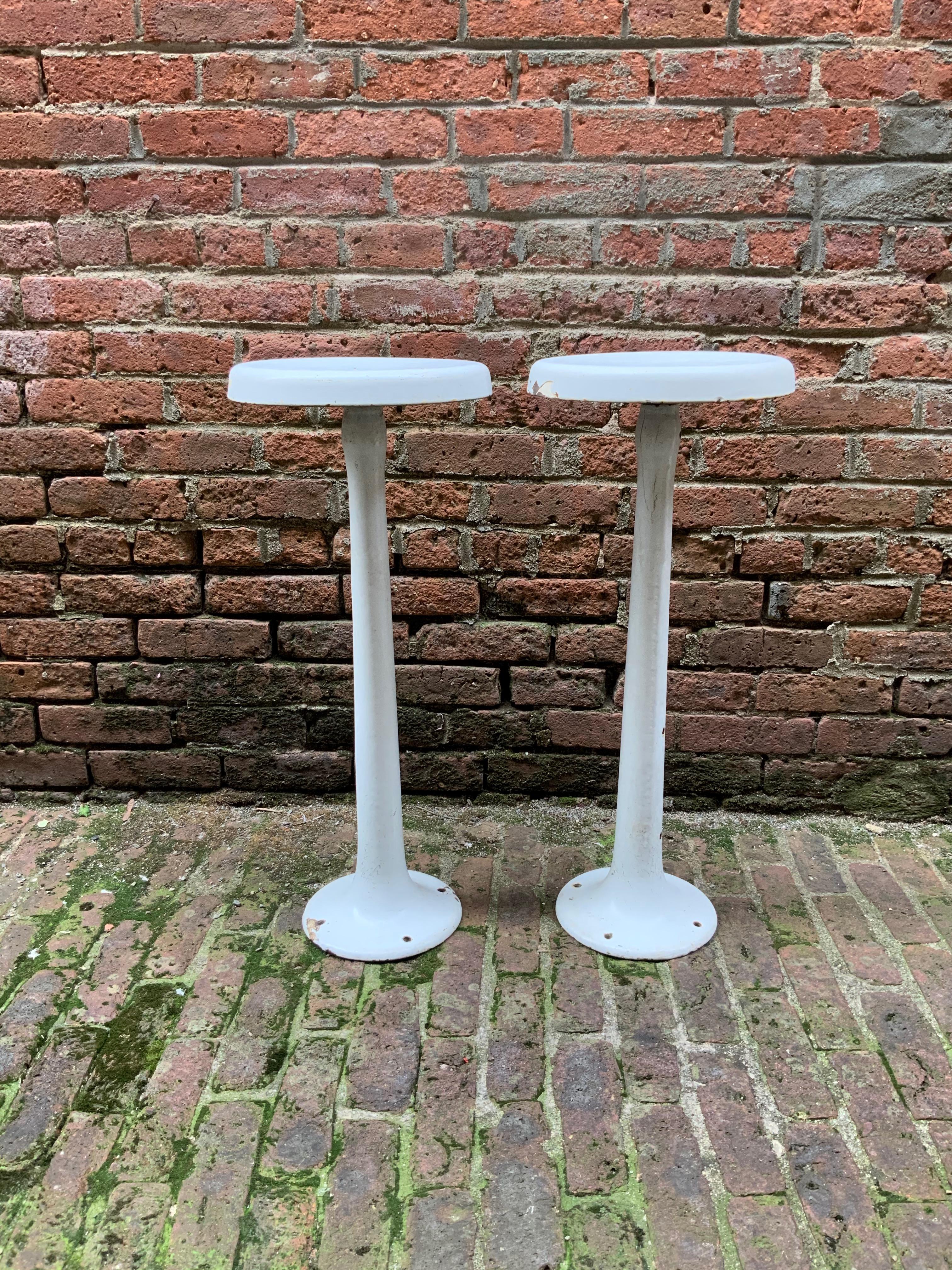 White porcelain enamel and cast iron swivel bar stools, circa 1920-1930. The bases can be fastened to the floor for stability. Good distressed condition with some rusting on the undersides and enamel chips (see photos). Possibly missing a footrest