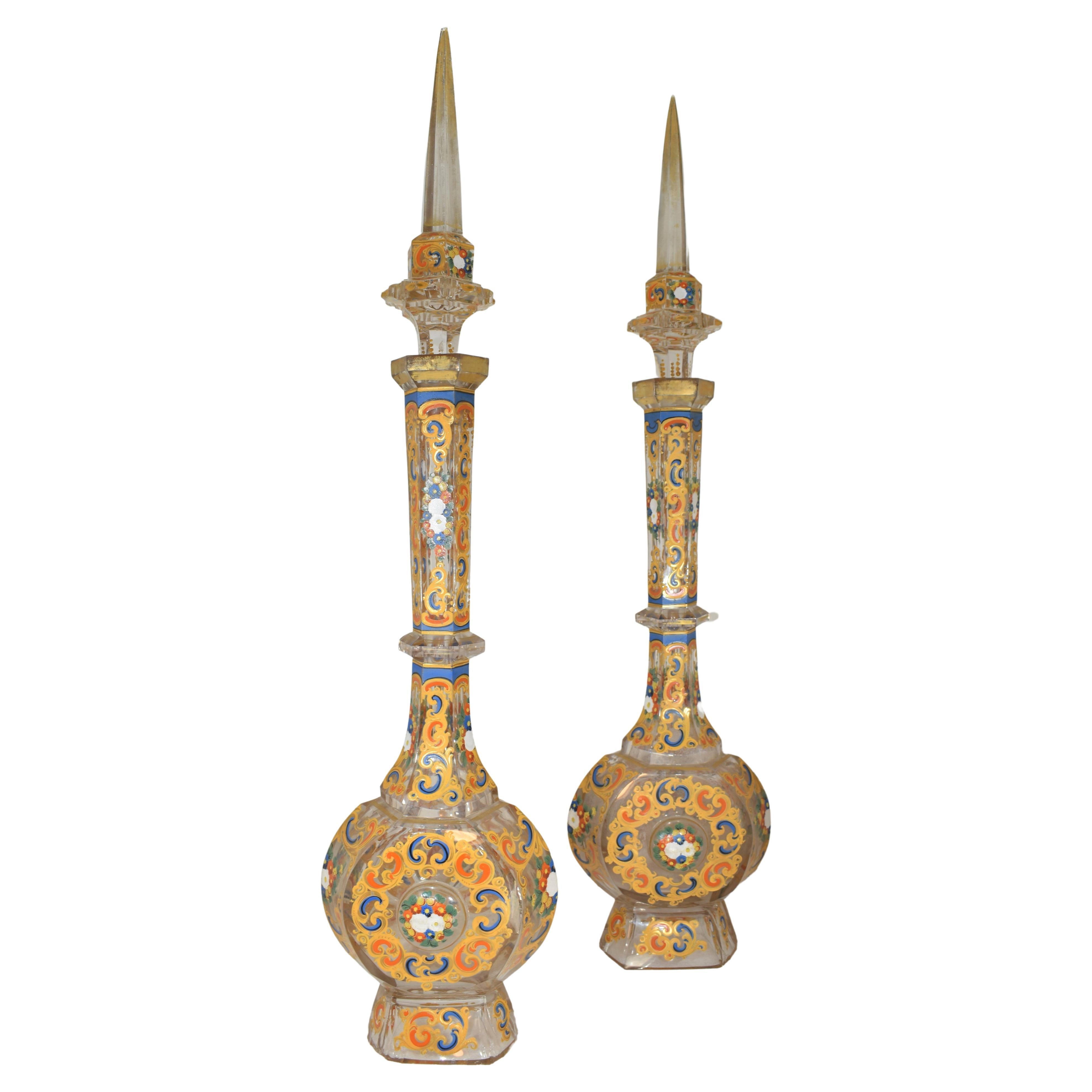 A pair of Bohemian enameled and cut clear-glass decanters and stoppers
Late 19th century
With flattened circular body and faceted knopped neck, the stopper with spire finial, enamelled with bouquets and scrolls, chips on base rims and on one