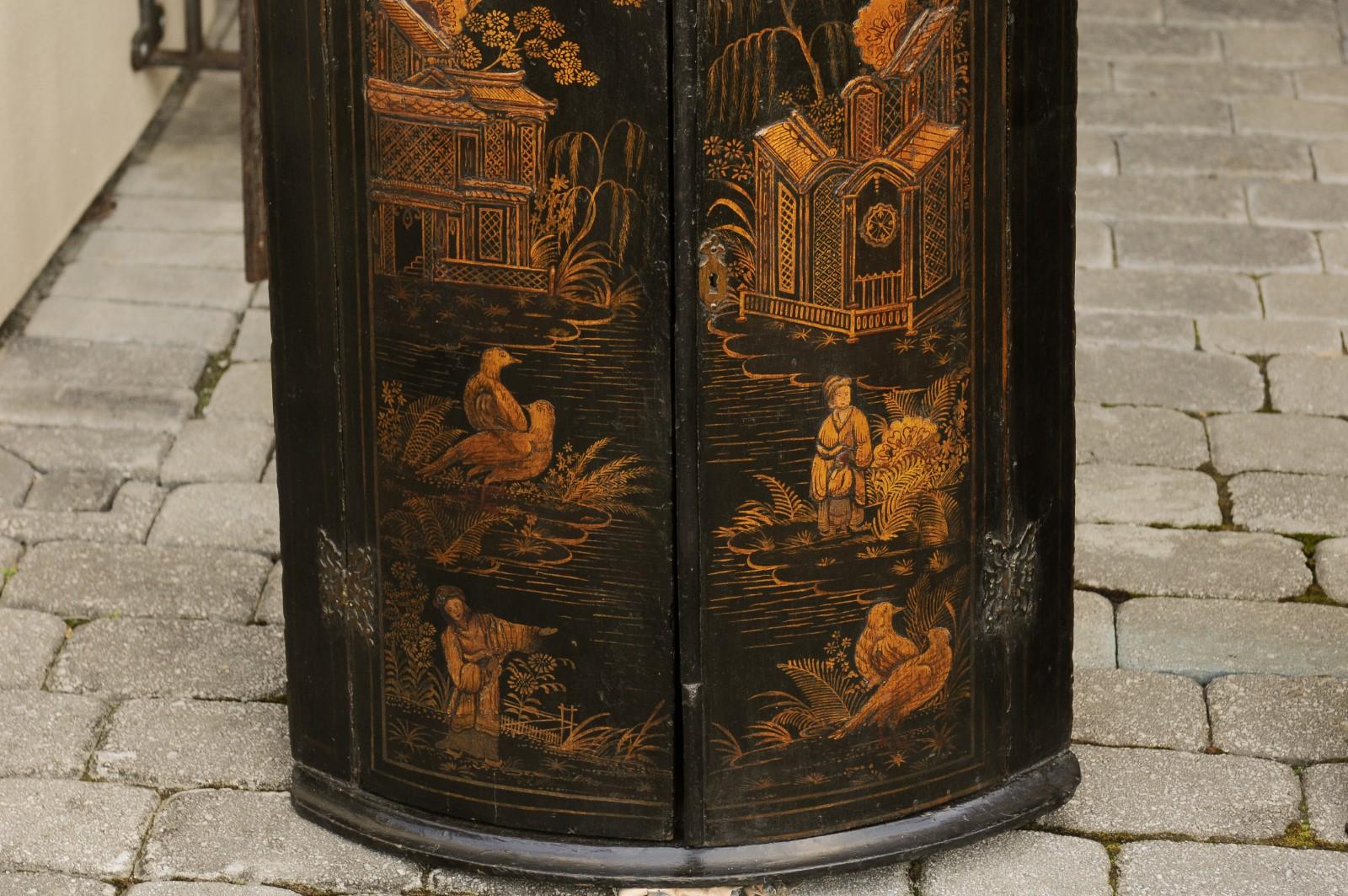 A pair of English corner cabinets from the late 18th century, with chinoiserie motifs. Born in England during the reign of King George III, each of this exquisite pair of corner cabinets features a black and gold décor, presenting traditional