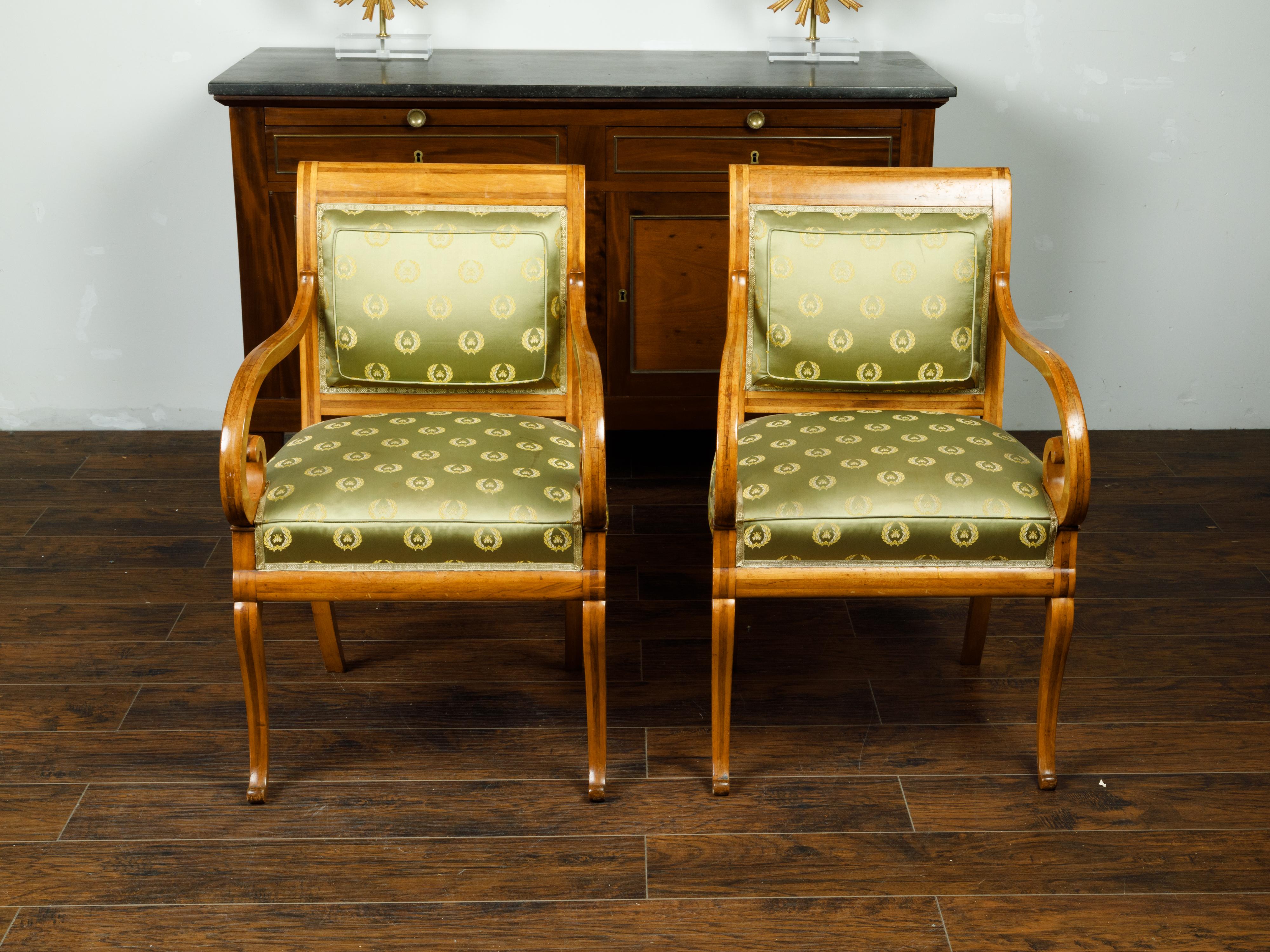 A pair of English Regency walnut armchairs from the mid 19th century, with large scrolling arms and green upholstery. Created in England during the second quarter of the 19th century, each of this pair of armchairs features an out-curving back