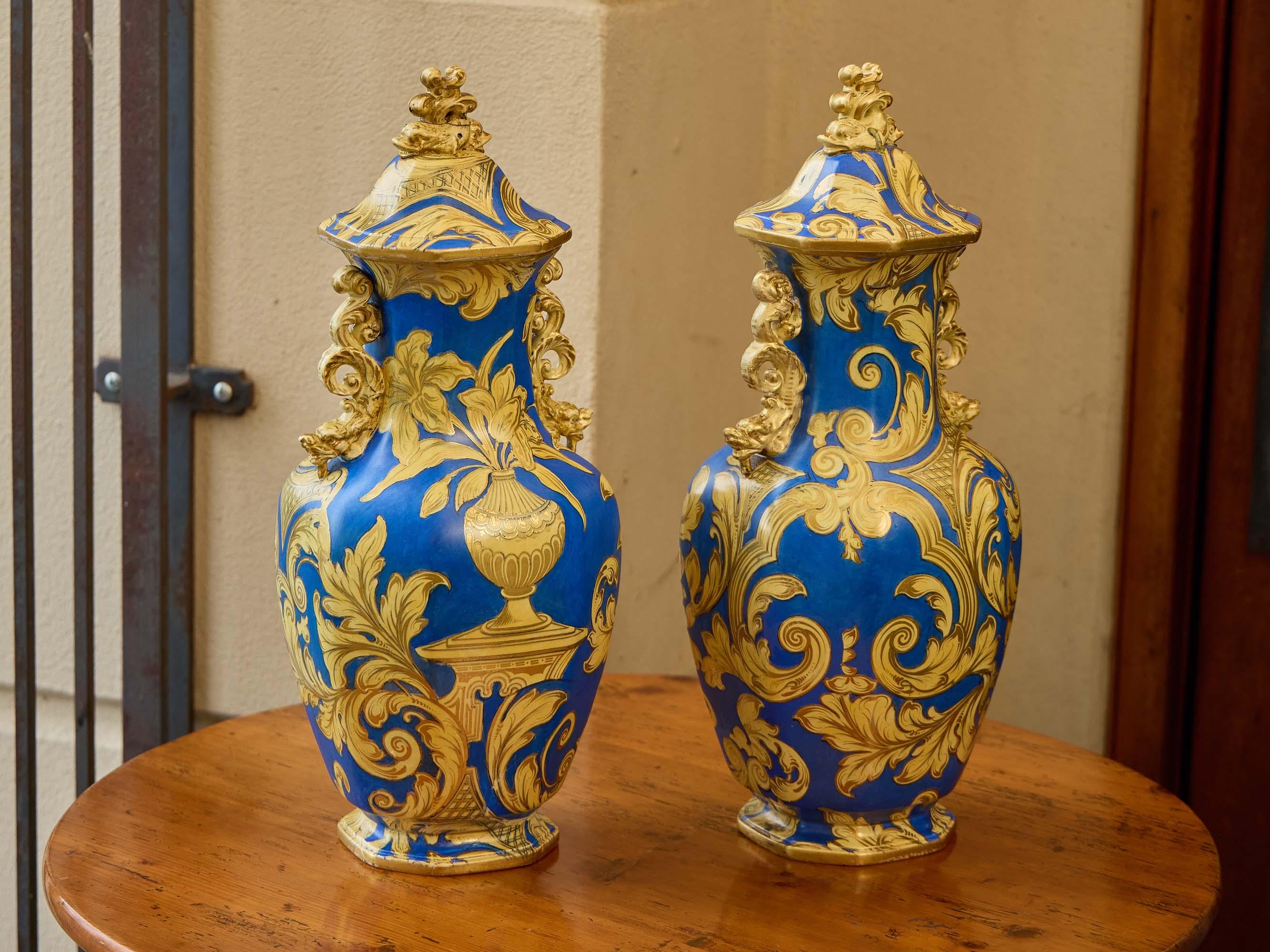 A striking pair of English Mason’s Ironstone lidded vases dating to circa 1840, richly decorated in cobalt blue and gilt. Exemplifying the bold neoclassical revival style of early Victorian ceramics, these tall urn-form vases feature exuberant