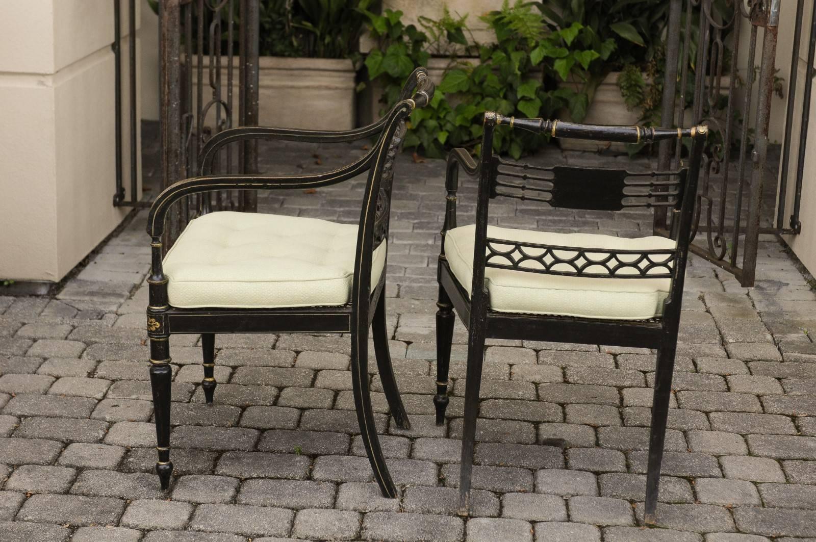 A pair of English Regency style ebonized wood open armchairs from the mid-19th century, with gilded accents, pierced backs and new custom-made cushions. Each of this pair of English armchairs features an elegant ebonized structure, delicately