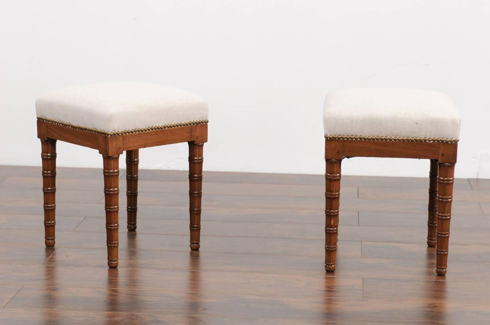 A pair of English faux-bamboo mahogany stools from the second half of the 19th century, with new upholstery and nailhead trim. Each of this pair of English stools features a linen-covered square seat, accented with a brass nailhead trim. Adorned