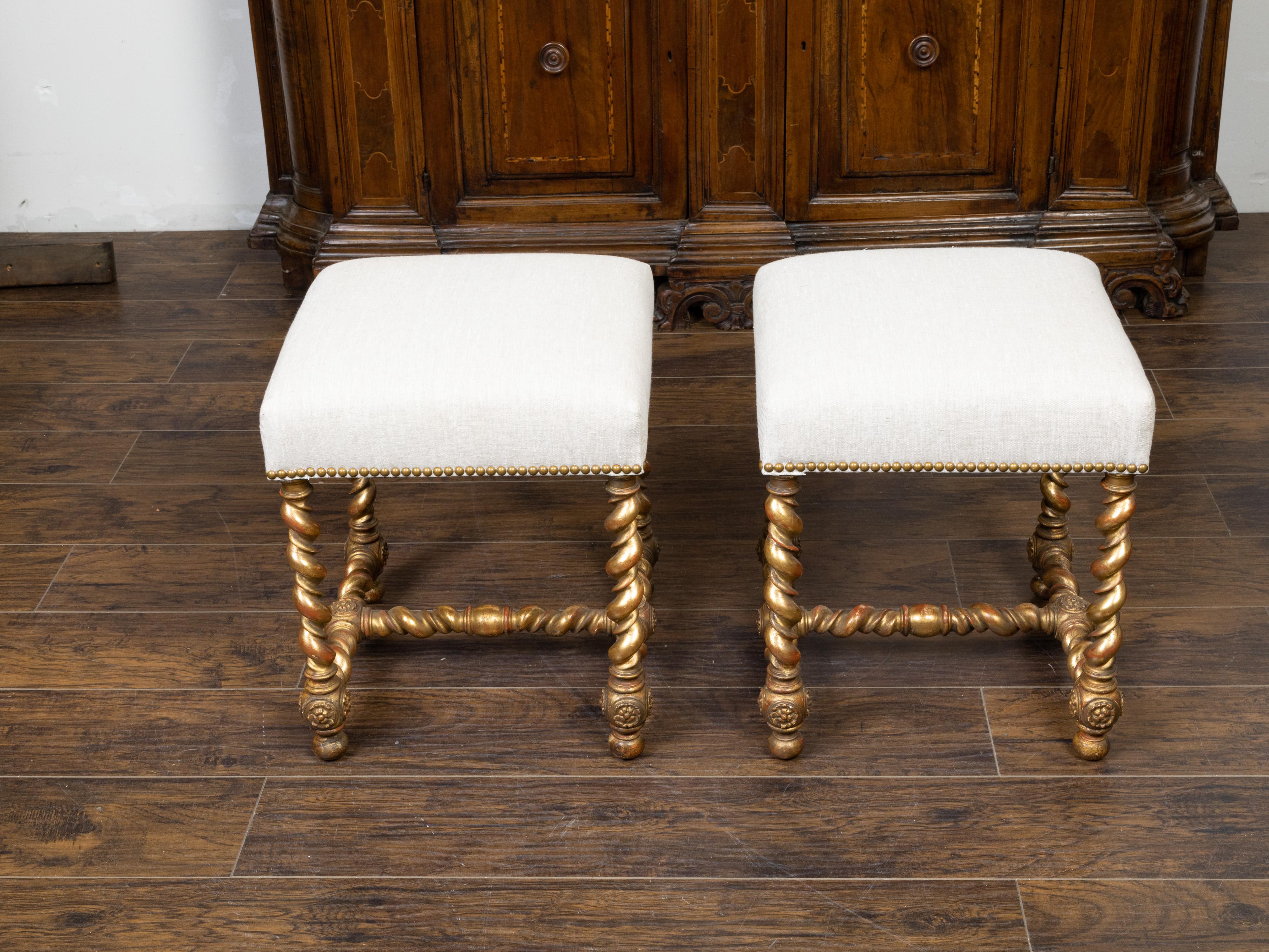 A pair of English giltwood barley twist stools from the late 19th century, with new upholstery. Created in England during the last quarter of the 19th century, each of this pair of stools features a square top newly reupholstered with a neutral