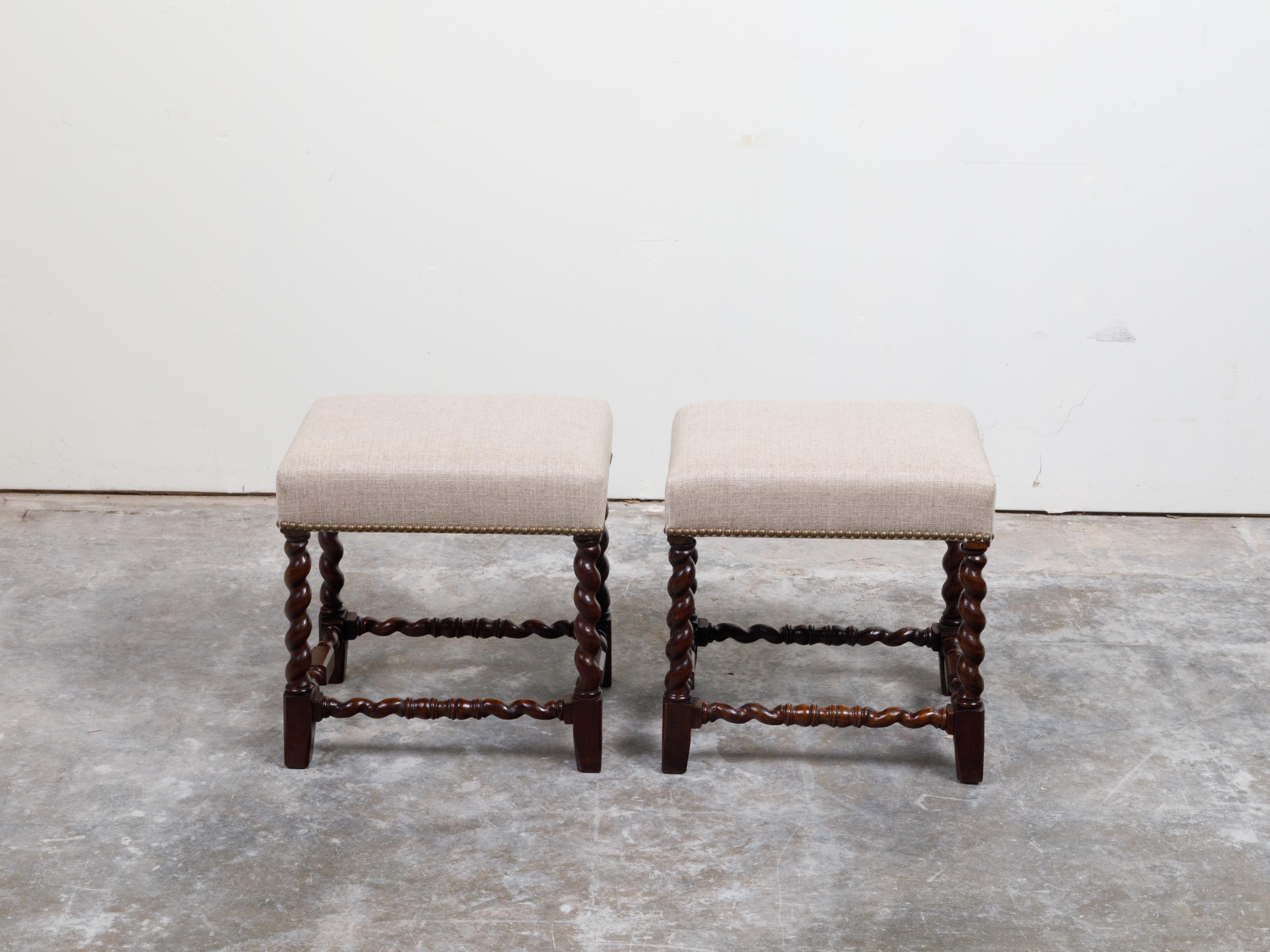 A pair of English oak stools from the early 20th century, with barley twist bases and new upholstery. Created in England during the early years of the 20th century, each of this pair of oak stools features a rectangular top newly reupholstered with
