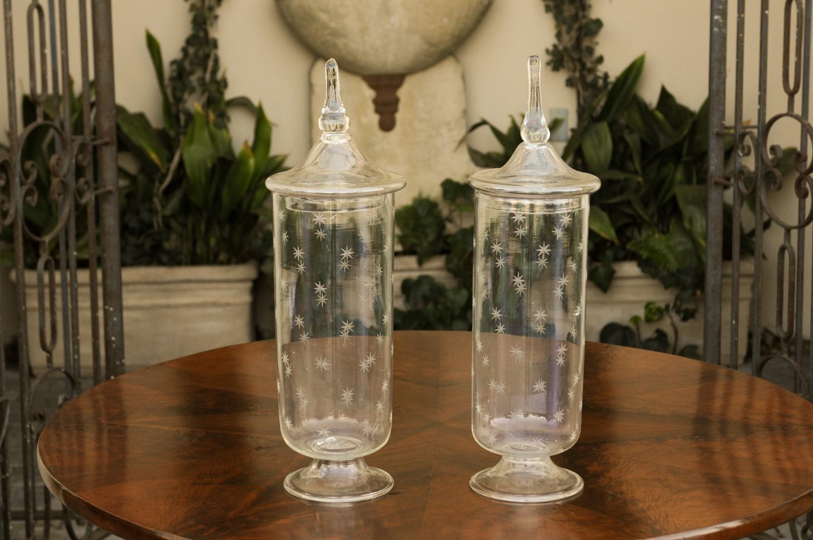 A pair of English Edwardian period tall glass lidded jars from the early 20th century, with circular bases and star motifs. Born in England during the reign of King Edward VII, each of this pair of stylish glass jars features a conic lid with tall