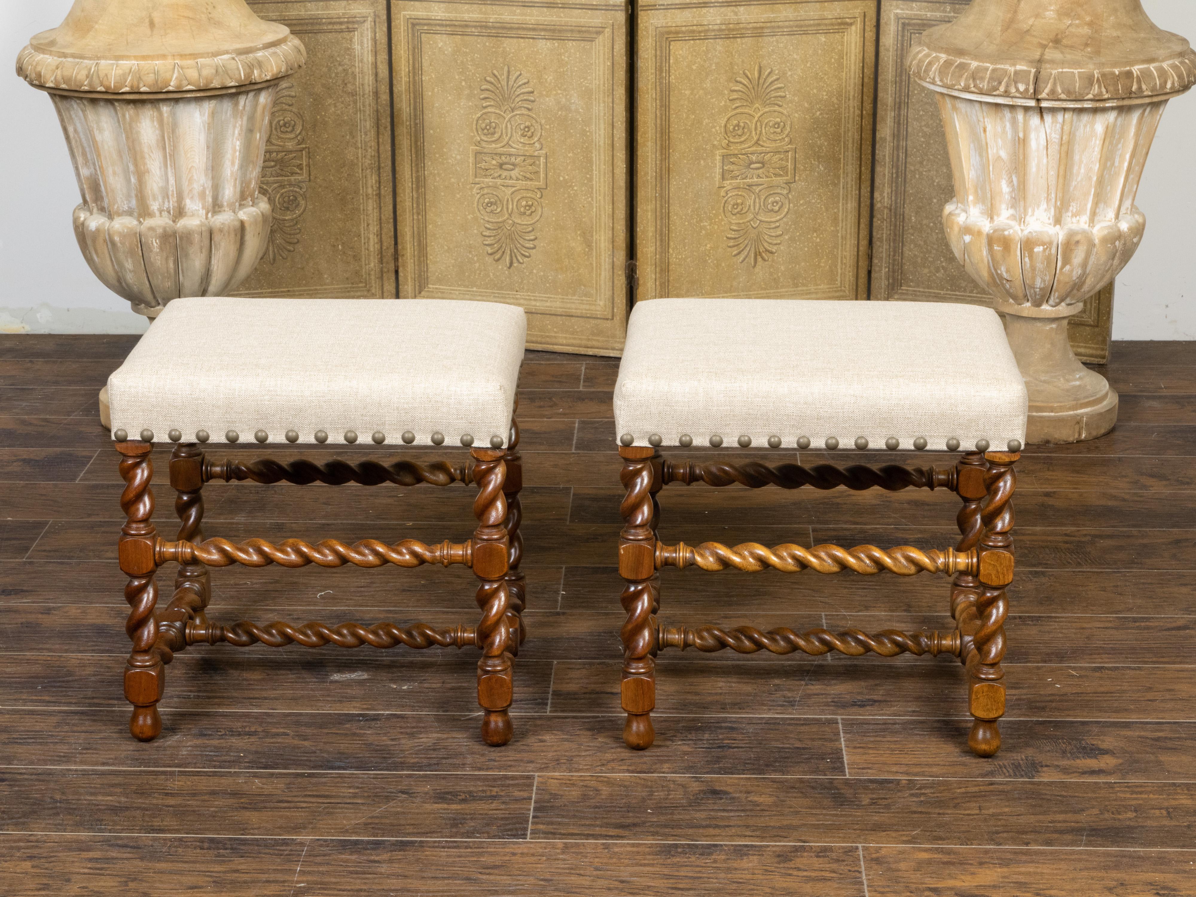 A pair of English oak stools from the early 20th century, with barley twist bases and new linen upholstery accented with a brass nailhead trim. Created in England during the vibrant Roaring Twenties in the first quarter of the 20th century, each of