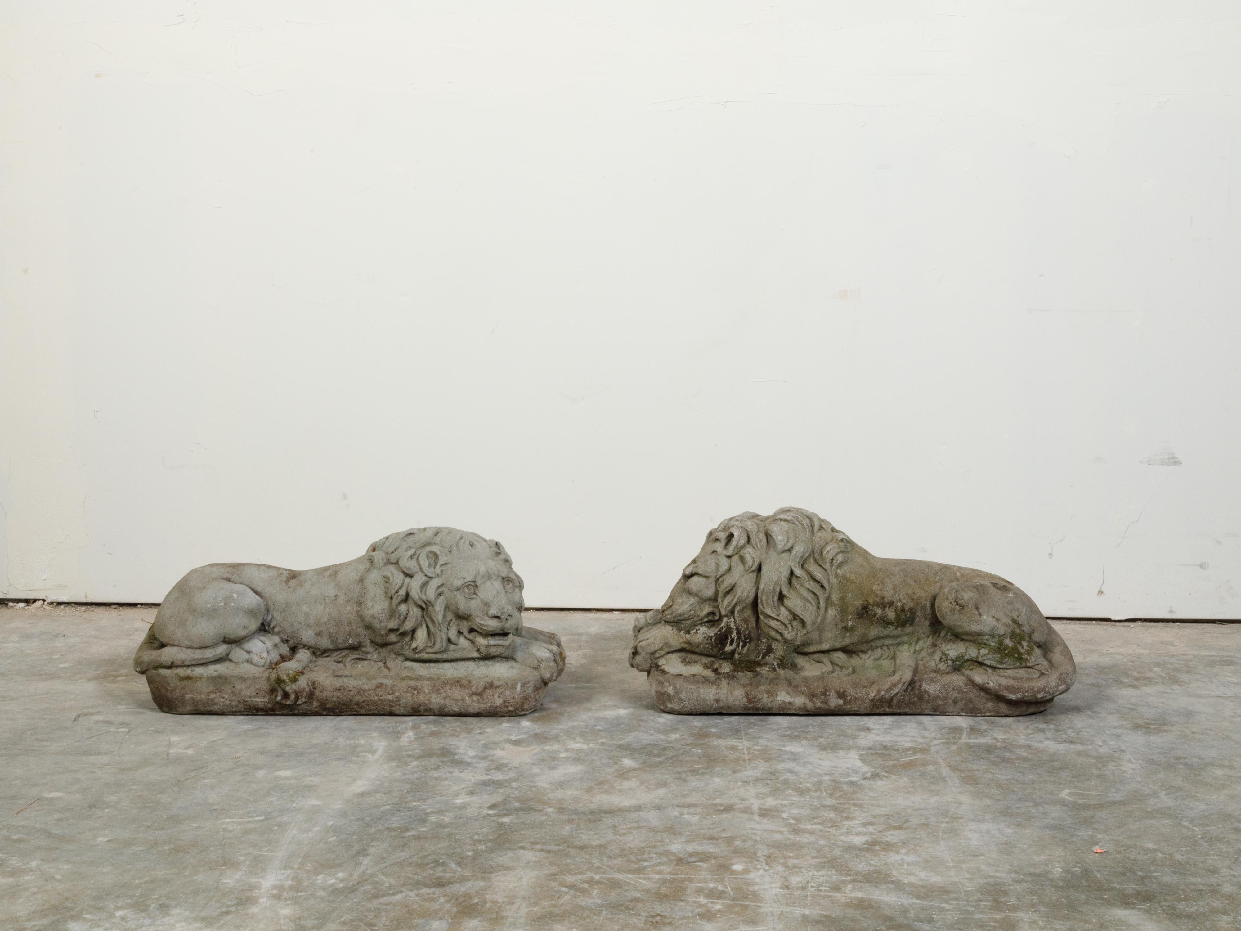A pair of English cast stone reclining lions statues from the early 20th century, on rectangular bases. Created in England during the first quarter of the 20th century, each of this pair of cast stone statues features a lion reclining on a
