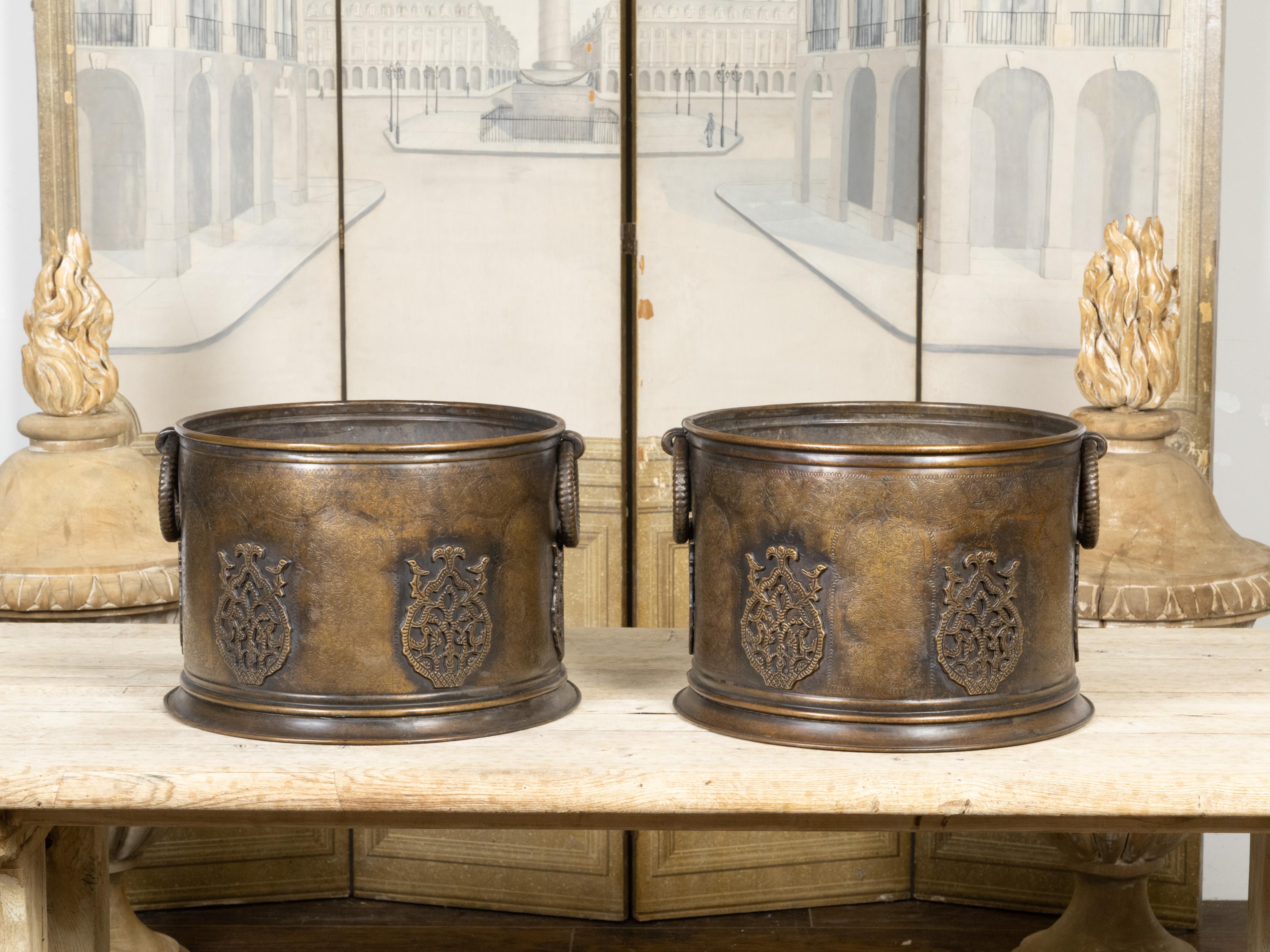 A pair of English copper cache-pot planters from the early 20th century, with ring pull handles, etched foliage and raised motifs. Created in England during the first quarter of the 20th century, each of this pair of copper cache-pot planters