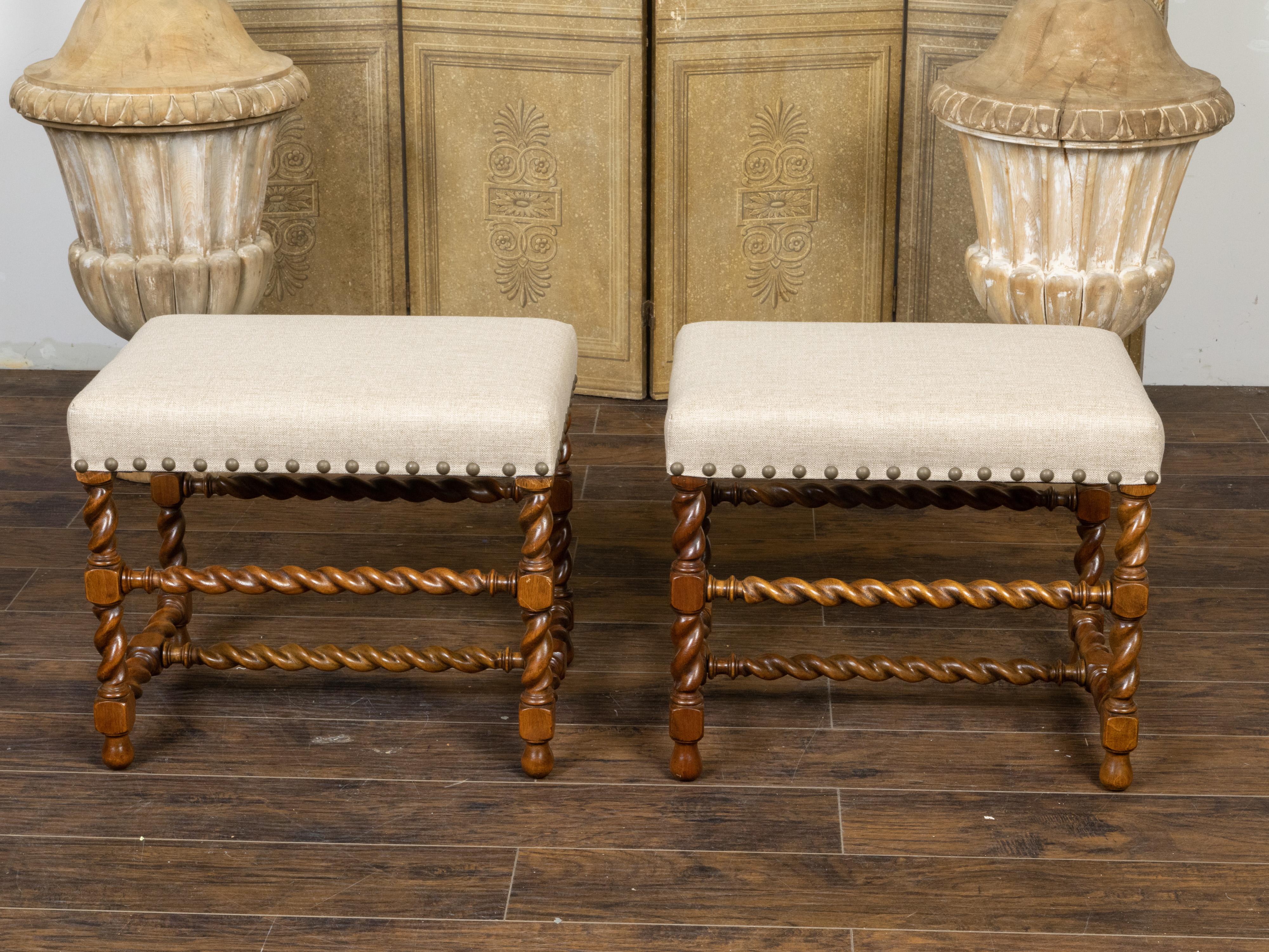 A pair of English oak stools from the early 20th century, with barley twist bases and new upholstery. Created in England during the first quarter of the 20th century, each of this pair of oak stools features a rectangular top newly reupholstered