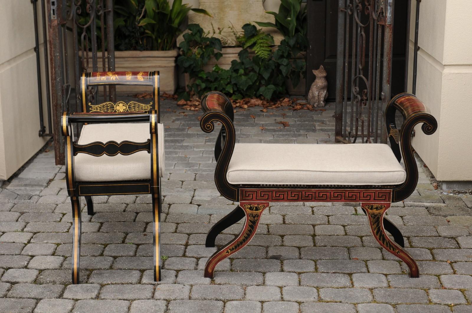 A pair of English neoclassical style benches from the mid-20th century, with ebonized wood, gilt and painted accents, Greek key frieze and new upholstery. Each of this exquisite pair of English benches features two graceful out-scrolled arms,