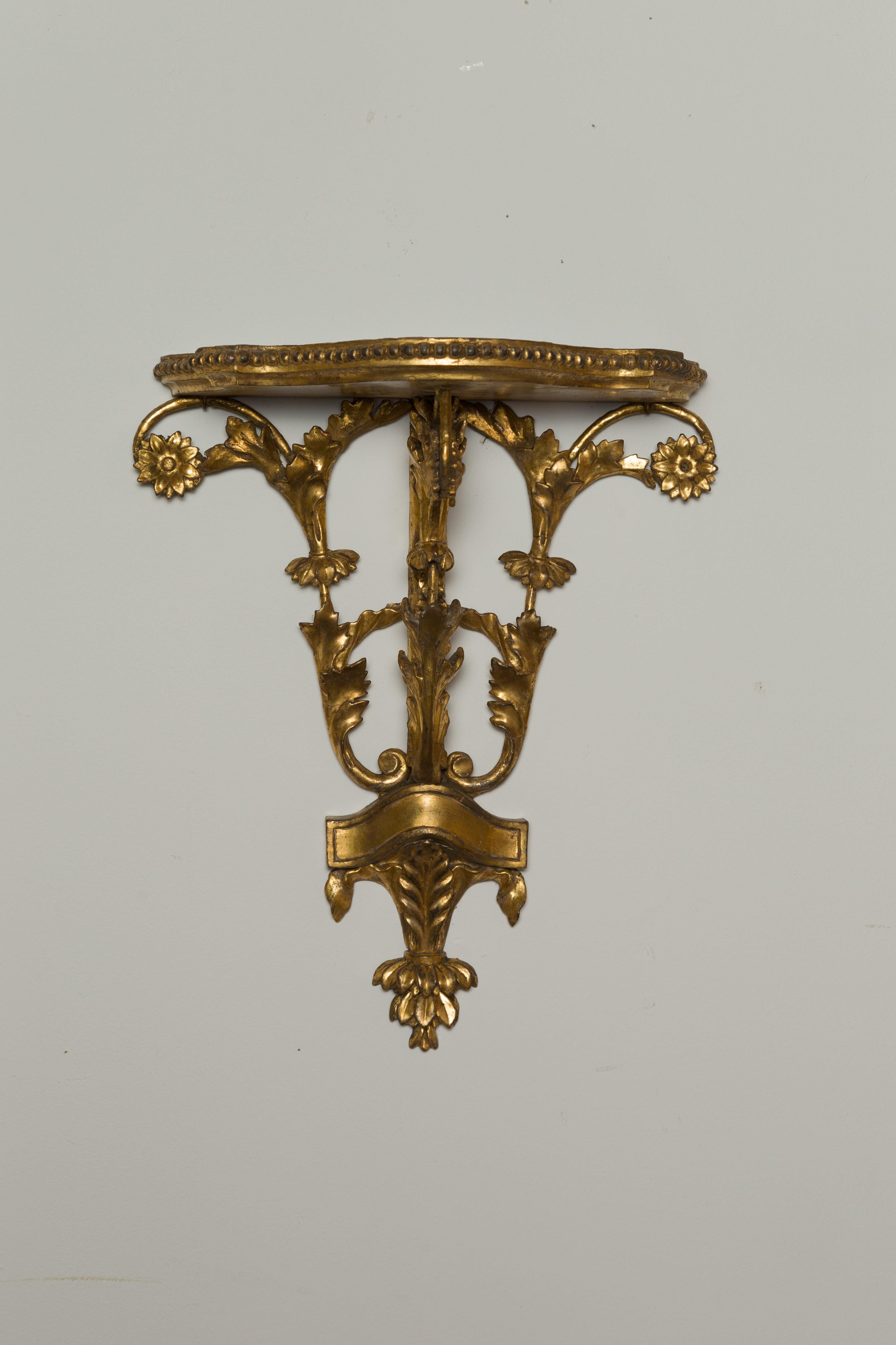 A pair of English carved giltwood brackets from the 19th century, with scrolling foliage and flowers. Created in England during the 19th century, each of this pair of wall brackets charms us with its giltwood structure showcasing a shaped top