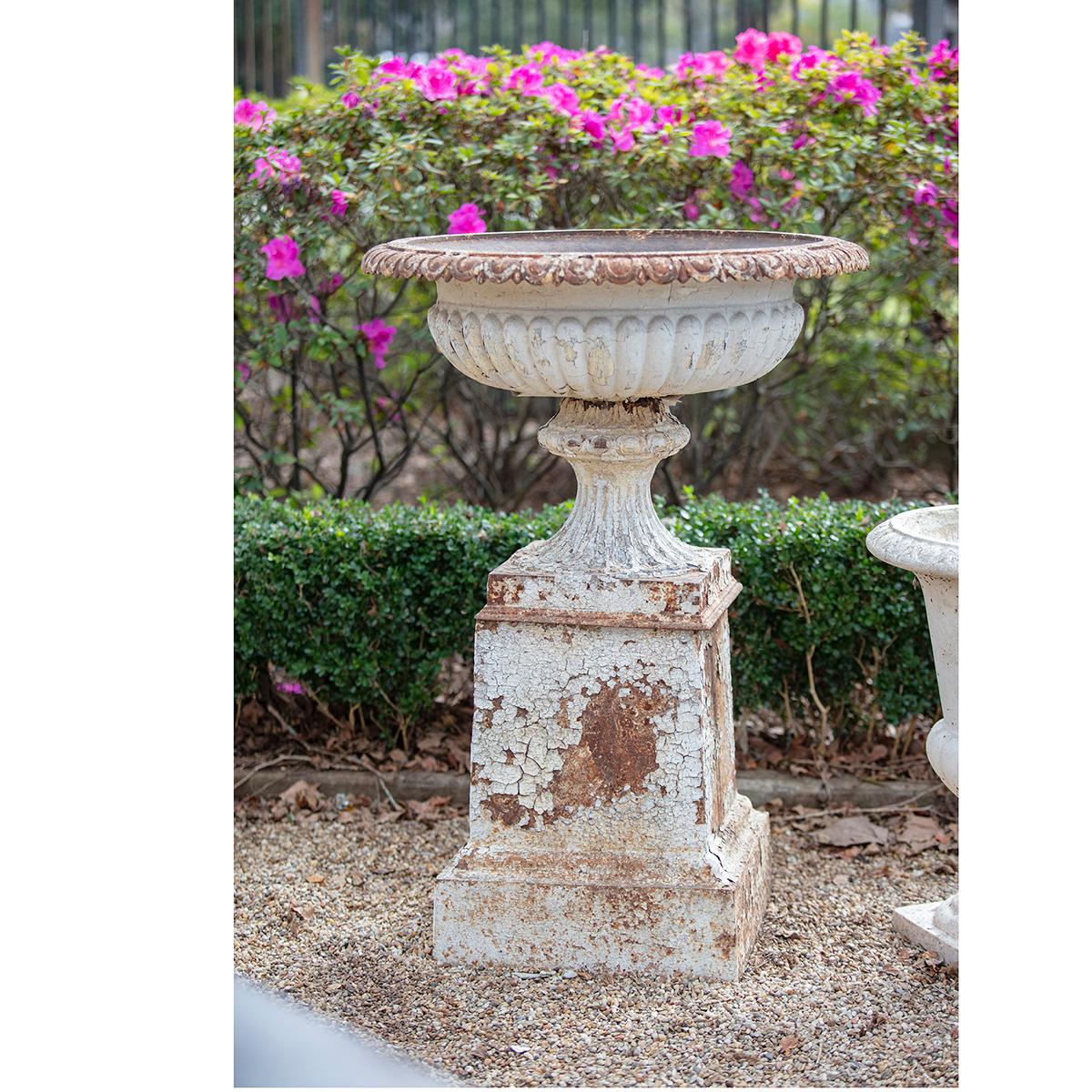 Pair of grand cast iron garden urns atop original cast iron bases in traditional English style. The urns are beautifully decorated and have a great patina – missing paint throughout and rust add to the wonderful finish. Make a statement with these