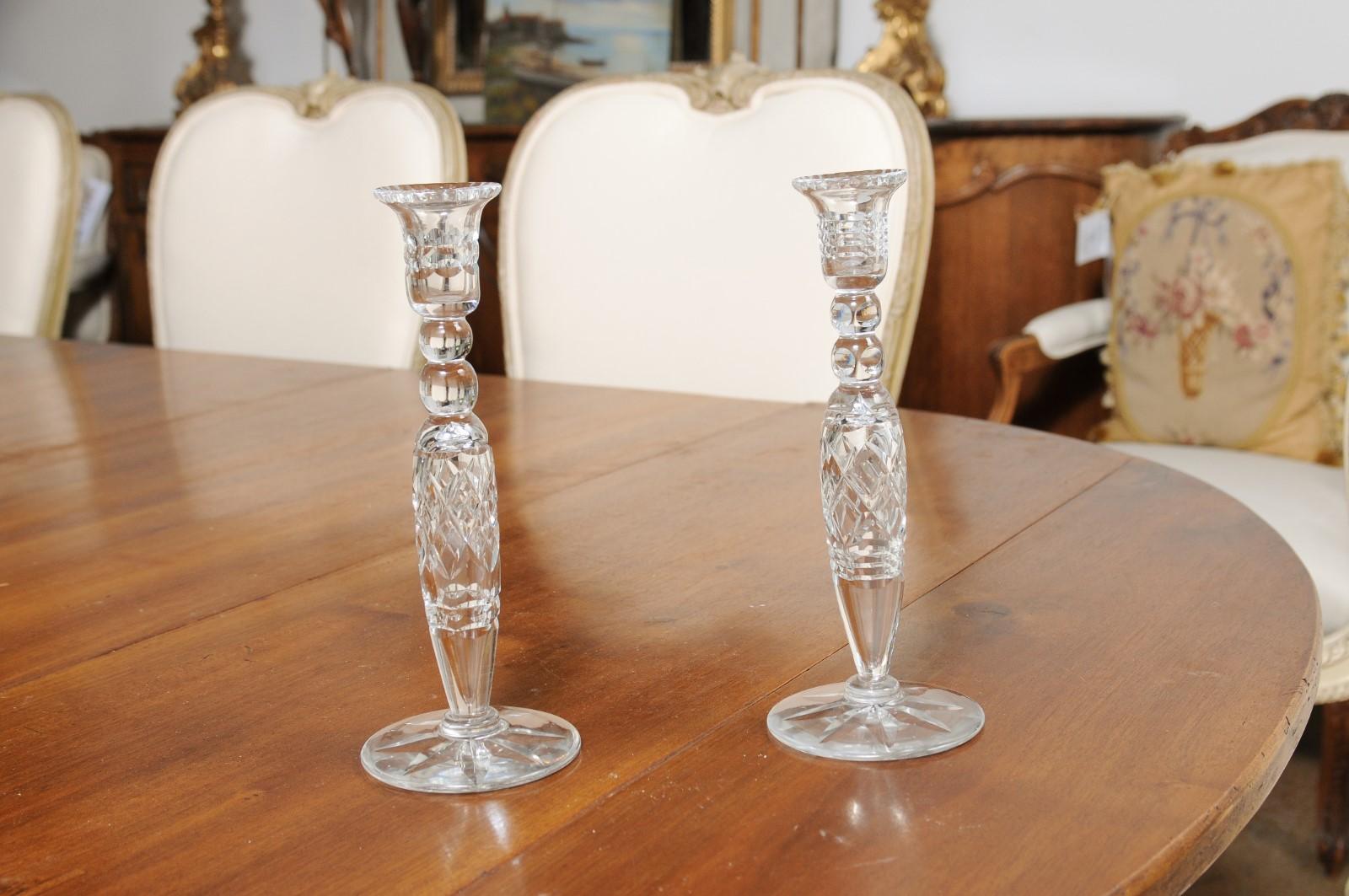 A pair of English crystal candlesticks from the 19th century, with cut diamond motifs. Created in England during the 19th century, each this pair of Victorian candlesticks features a slender body adorned with cut diamond motifs and spheres. Raised