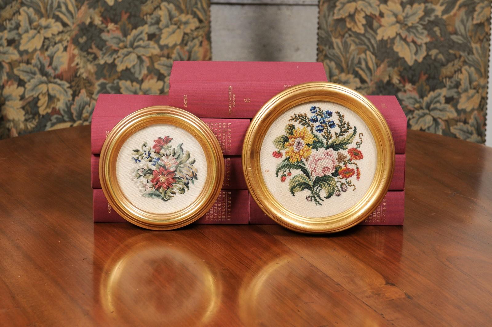 A pair of English Victorian period needlepoint tapestry floral wall hangings from the 19th century, in gilded circular frames. Originally found in Cornwall, each of this pair of wall hangings features a bouquet of pink, red and yellow flowers with