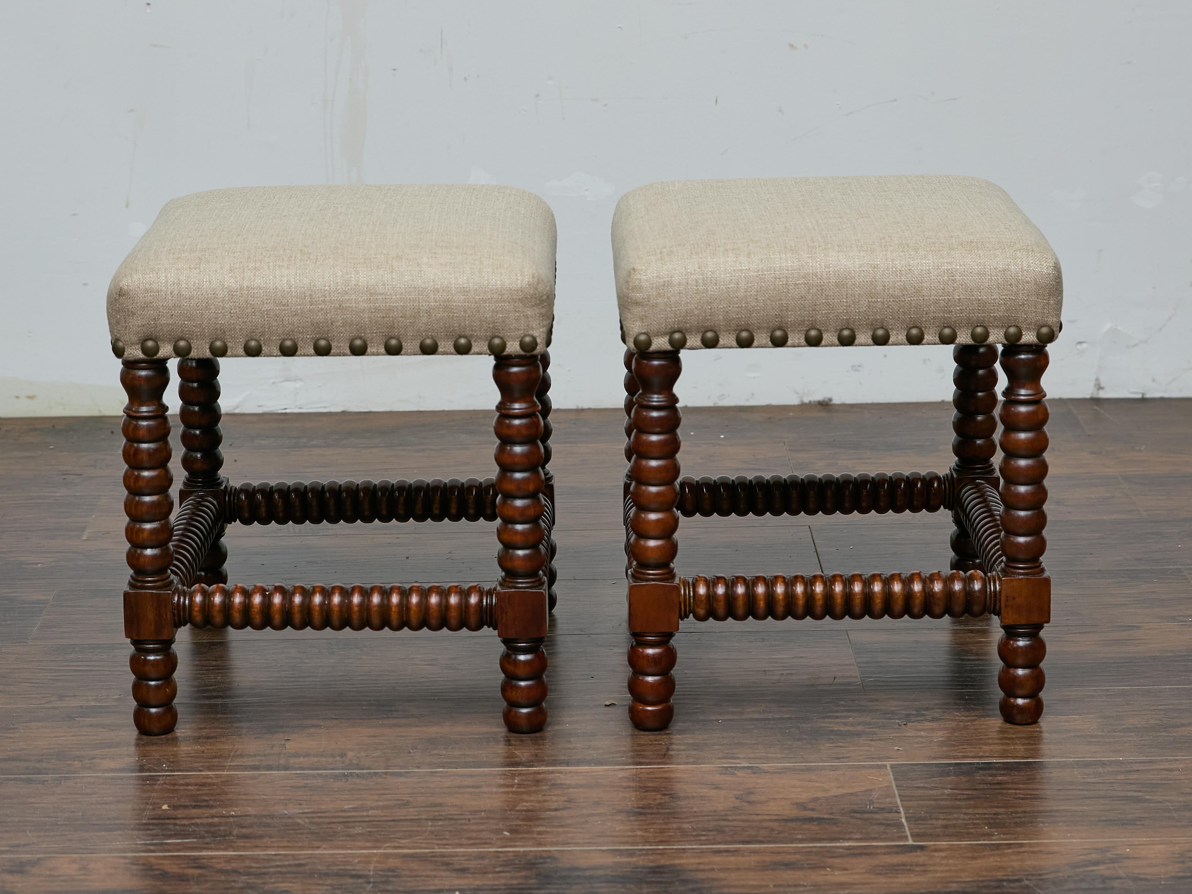 Questa coppia di sgabelli inglesi del XIX secolo ha un carattere senza tempo grazie alle gambe a spola tornite a mano e alle cornici in legno duro. Rivestite di recente in un tessuto di lino personalizzato, offrono un raffinato contrasto tra la