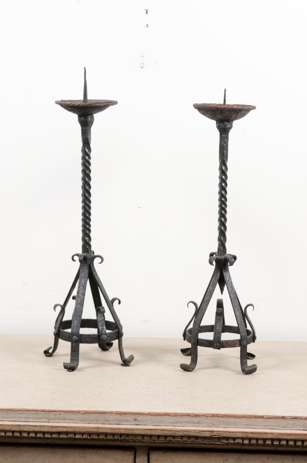 A pair of English iron candlesticks from the 19th century, with twisted accents and scrolling feet. Born in England during the 19th century, each of this pair of iron candlesticks features a twisted central staff supporting a pricket, while the