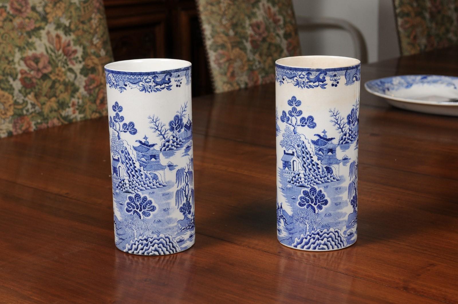 A pair of English blue and white Mason's patent ironstone vases from the 19th century, with chinoiserie decor depicting two fishermen on a bridge surrounded by willow patterns. Born in England during the 19th century, each of this pair of