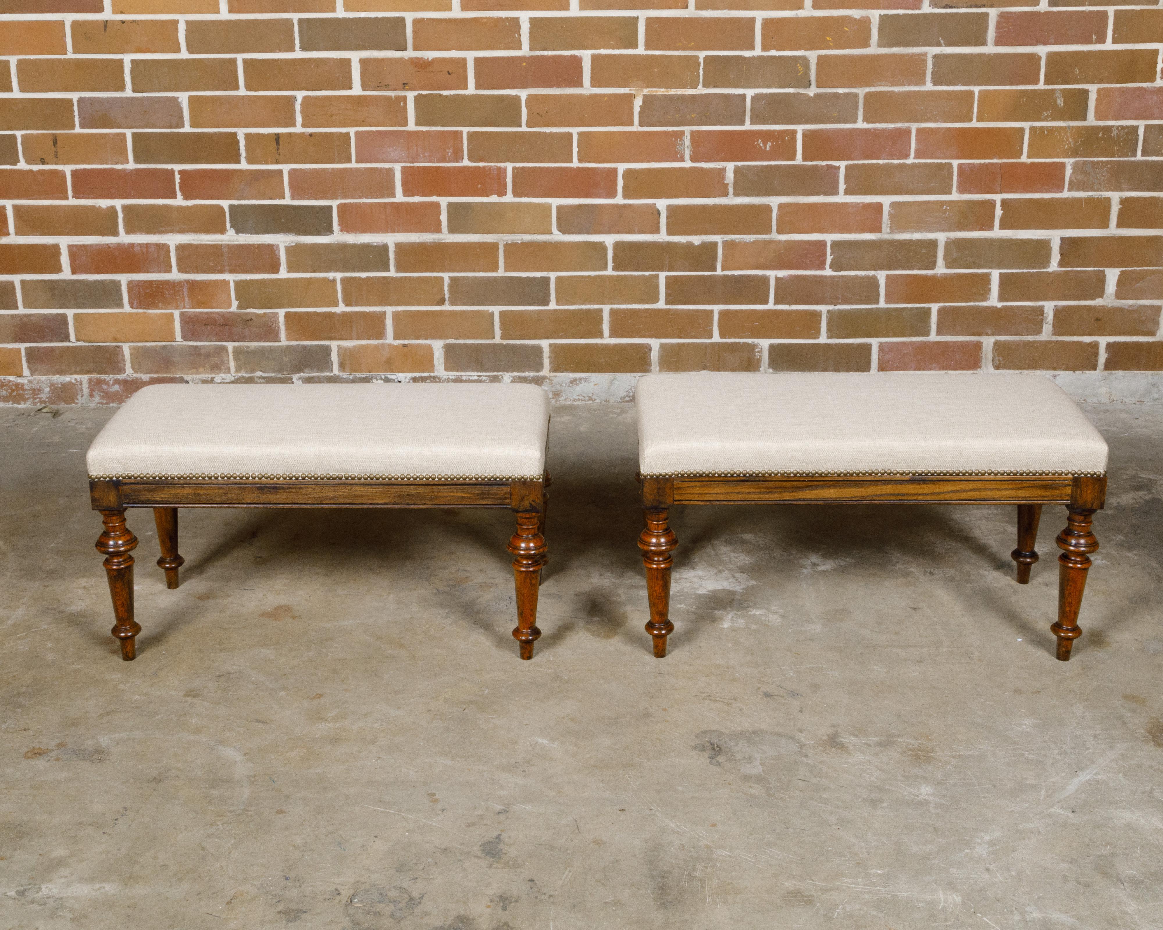 A pair of English oak rectangular stools from the 19th century with turned legs raised on arrow feet and custom upholstery. This captivating pair of English oak stools from the 19th century effortlessly marries the rustic charm of oak with the
