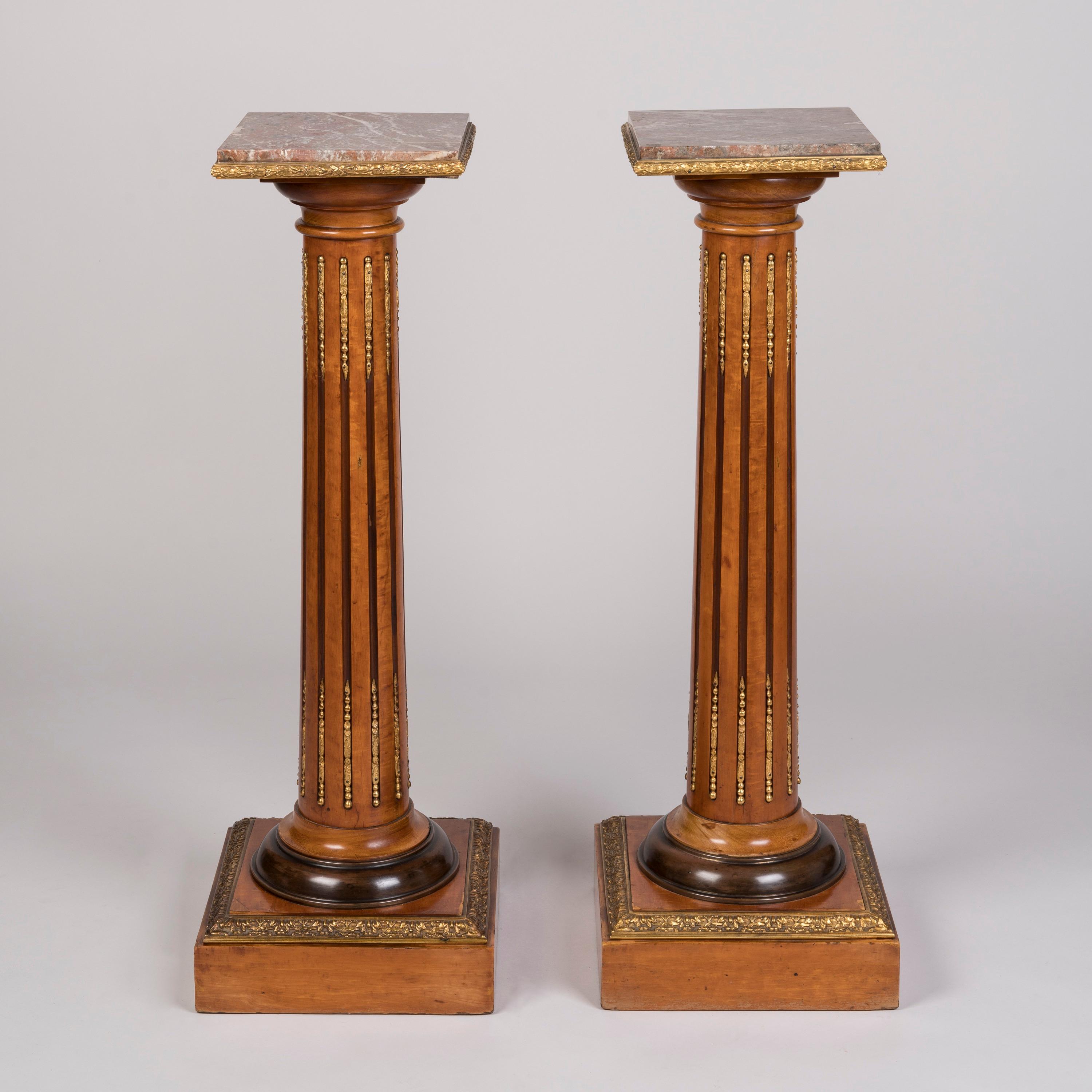 A Pair of Ormolu-Mounted Satinwood Pedestals

Veneered in satinwood and adorned with ormolu mounts, each pedestal supported on a square plinth base, the tapering columns fluted and with gilt bronze inserts, the turned capitals supporting a pink