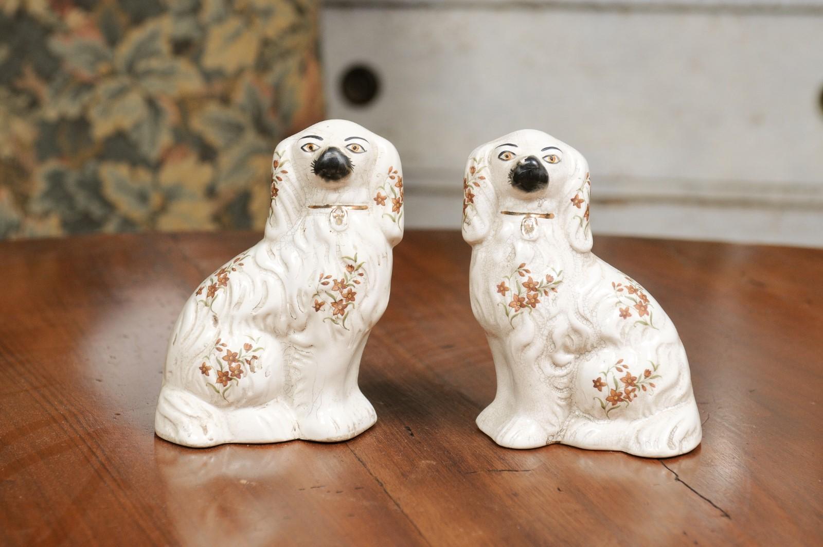 A pair of English Victorian period Staffordshire white dogs from the 19th century with hand-painted floral motifs. Created in England during the reign of Queen Victoria, this pair of Staffordshire features two sitting white toned Spaniel dogs,