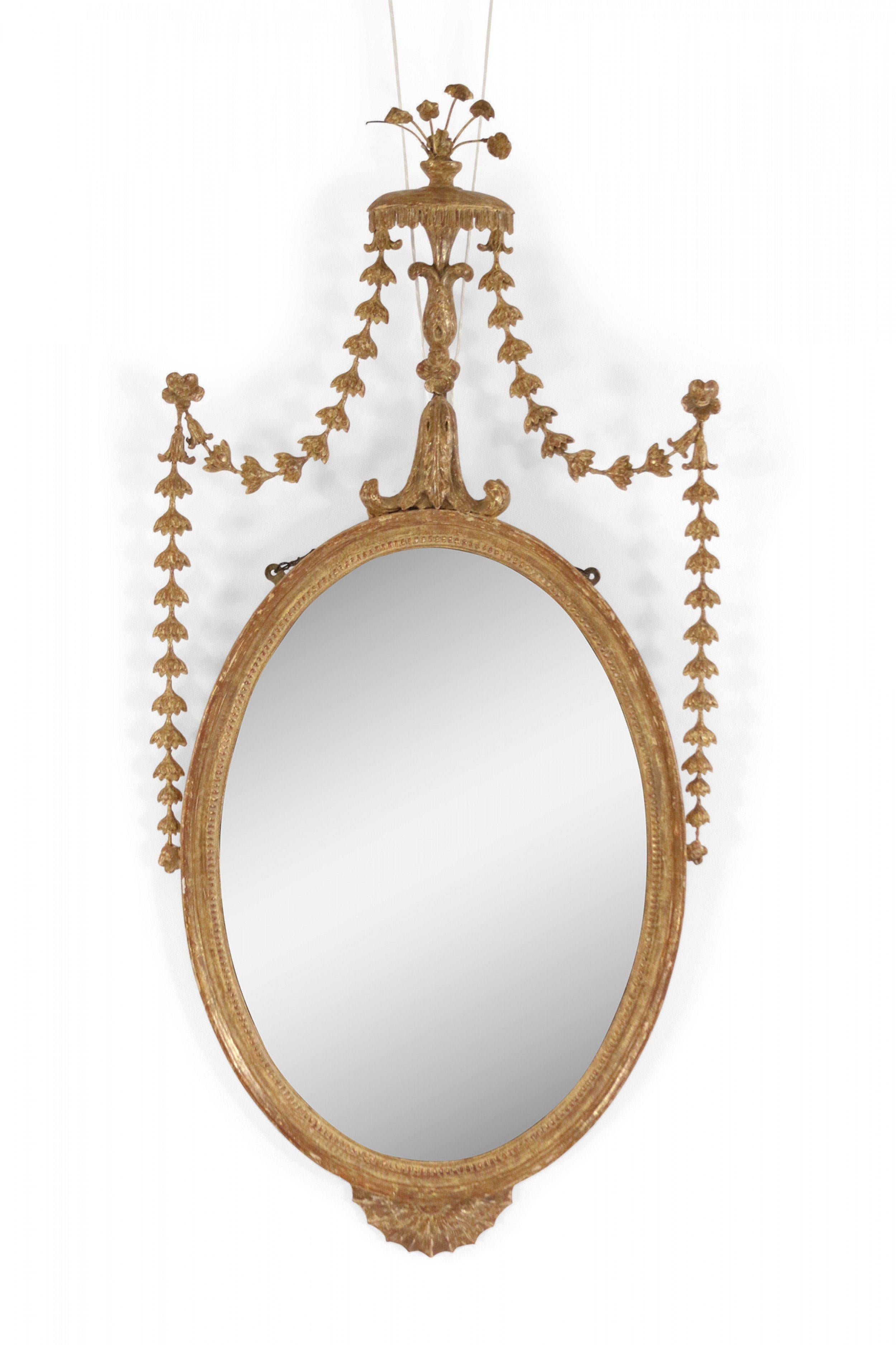Pair of English Adam style giltwood wall mirrors with carved oval frames and flower spray pediments.