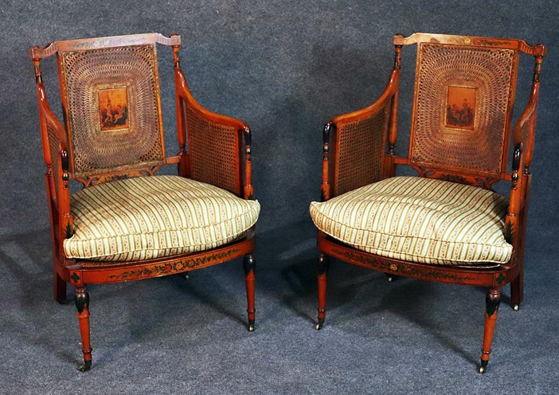 Pair of English Adams style paint decorated satinwood club chairs with front casters and caned seats, backs and sides.