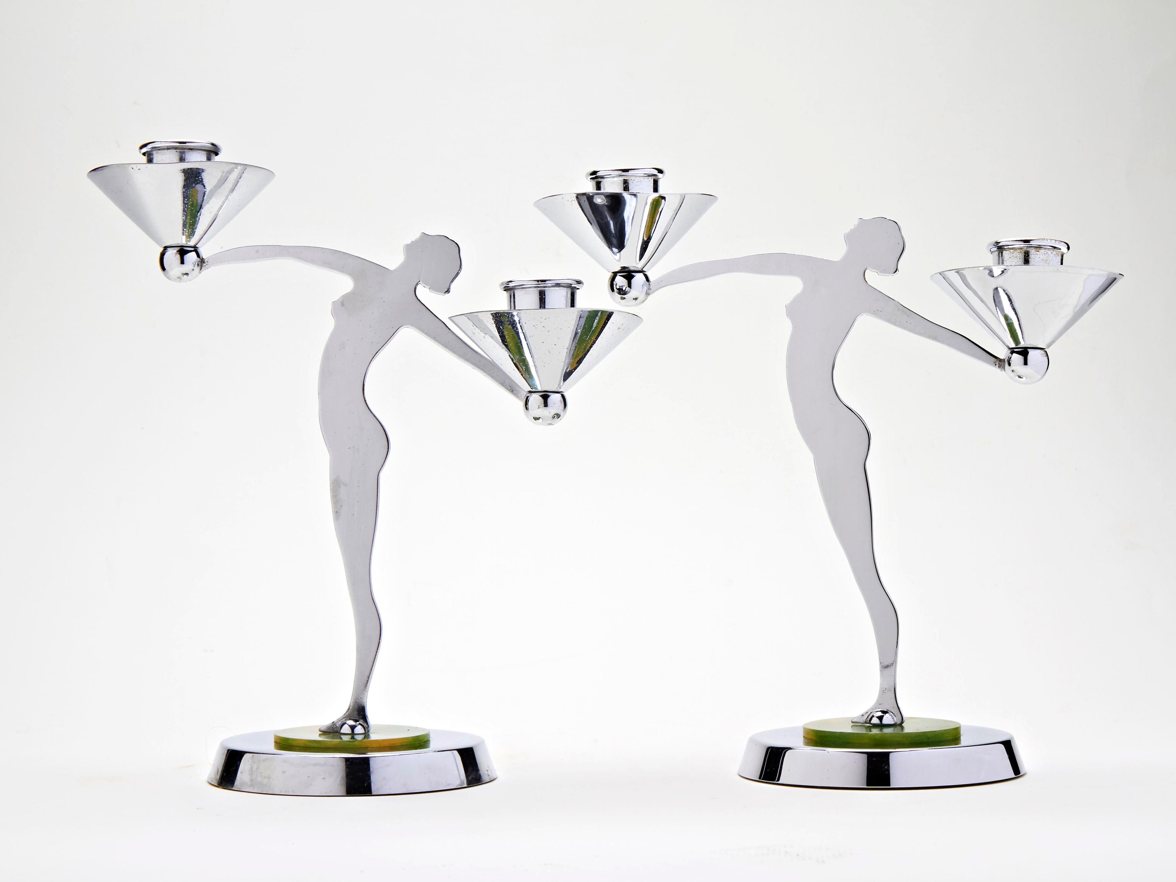 This stylish pair of English Art Deco chrome plated twin figural candleholders each feature a silhouetted figure of a nude female with her arms outstretched. In each hand they hold a chrome sphere supporting a candle socket with a conical chrome