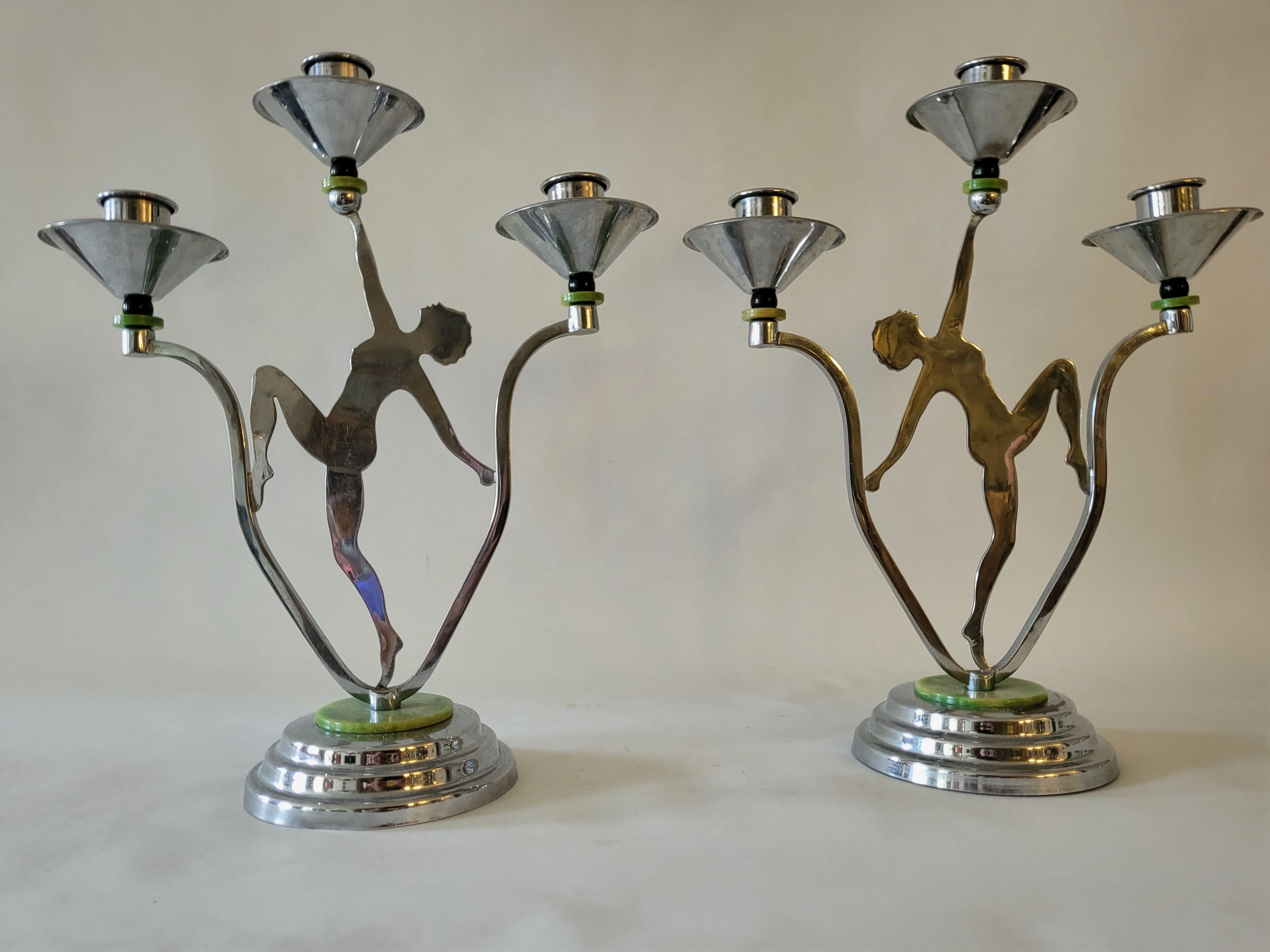 This rare pair of English Art Deco Chrome and Bakelite triple candle holders each feature a silhouette of a nude female holding aloft a marbled green Bakelite disk that supports a black Bakeite bead topped with a chrome candle socket and bobeche.