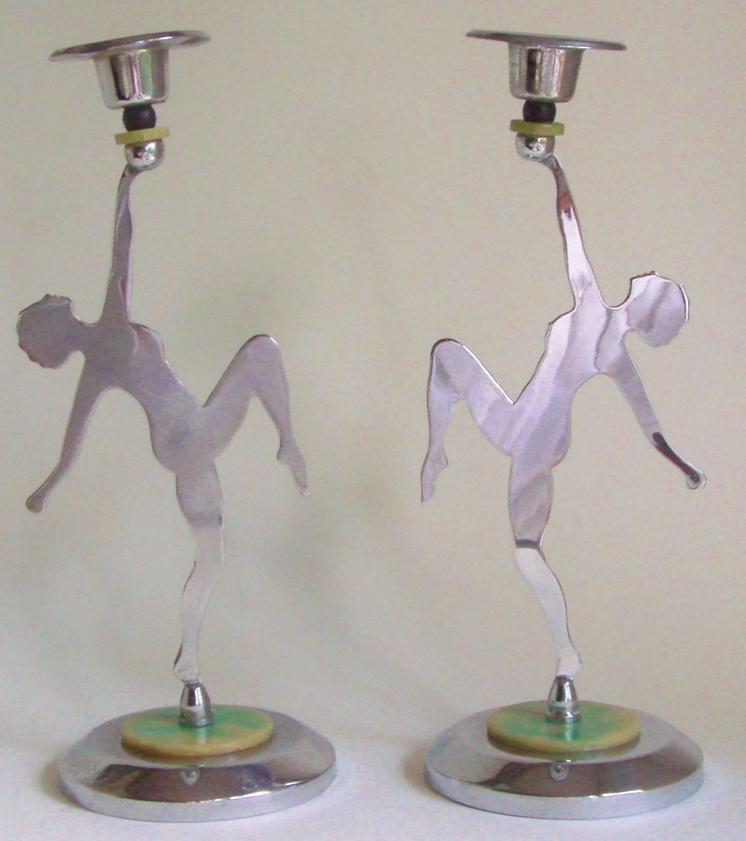 This pair of English Art Deco figural female nude candlesticks feature a circular chrome beveled edged base topped with a green marbled bakelite disk. Standing on this is a chrome stencil-cut silhouette of a naked female dancer. Her raised arm holds